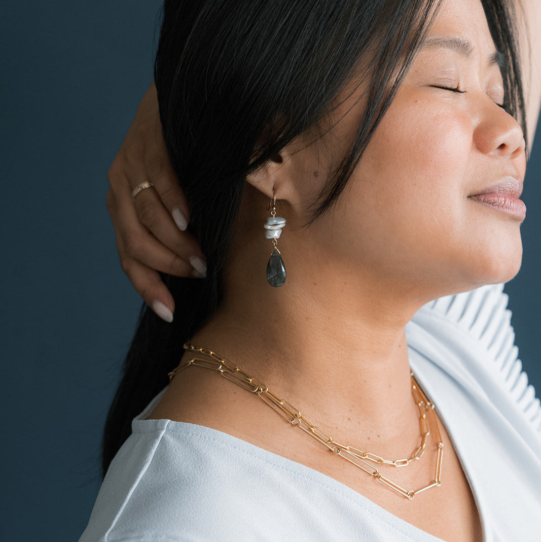 Close up of woman wearing a large statement earring with pearls and labradorite