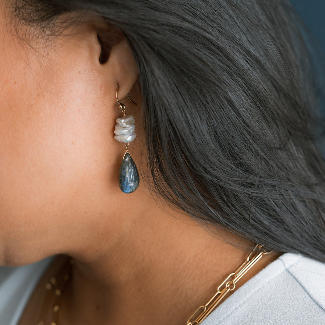 Close up of woman wearing a large statement earring with pearls and labradorite
