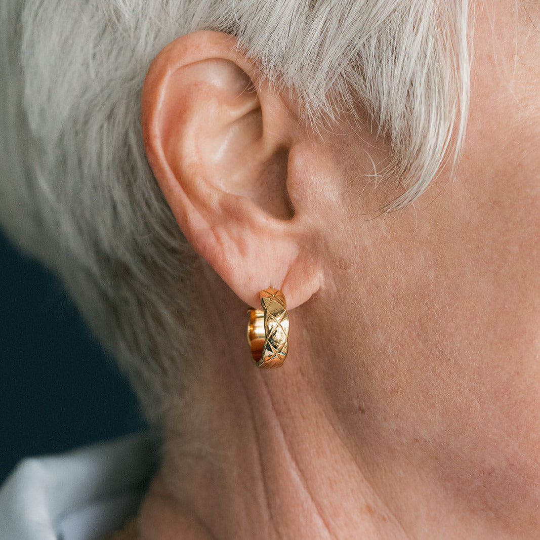 Woman with short silver hair wearing thick gold hoops on a dark blue background