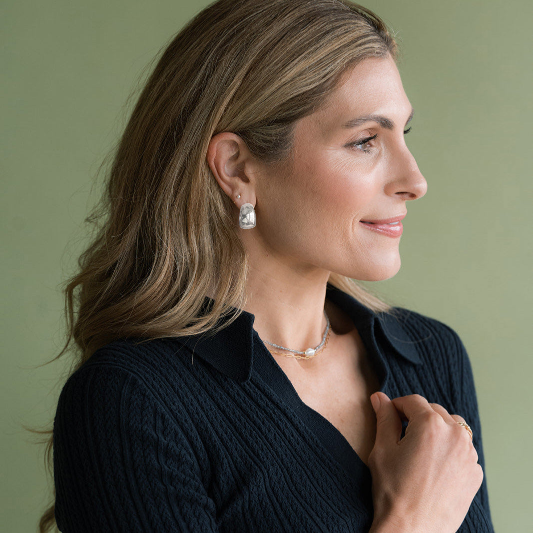 Woman wearing a navy sweater and chunky silver earrings against a green background