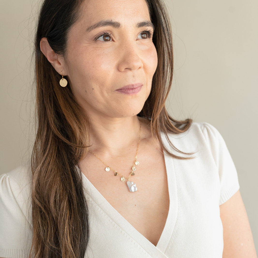 Woman wearing cream colored v-neck top with gold and baroque pearl jewelry