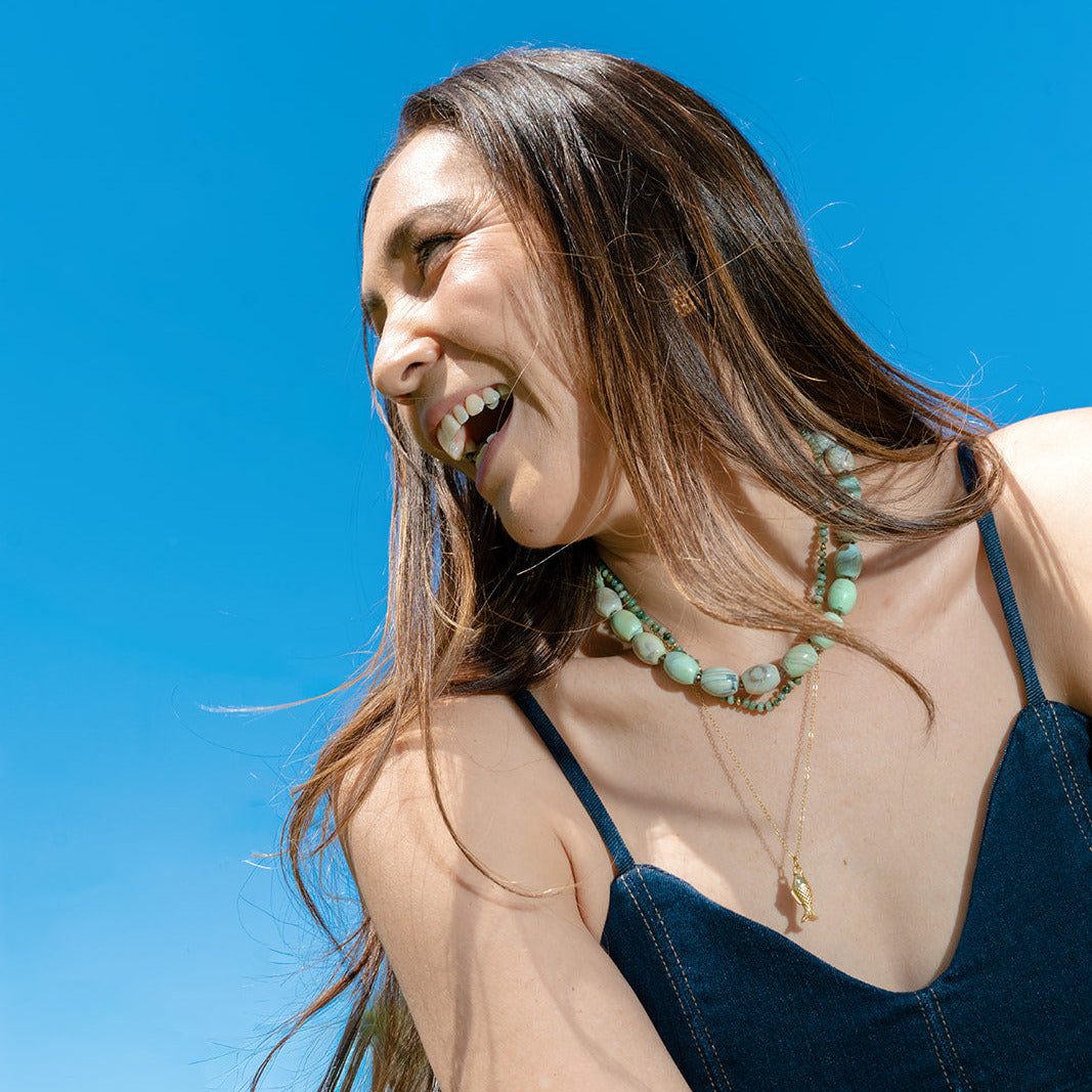 Woman laughing and wearing a teal agate necklace against a clear blue sky