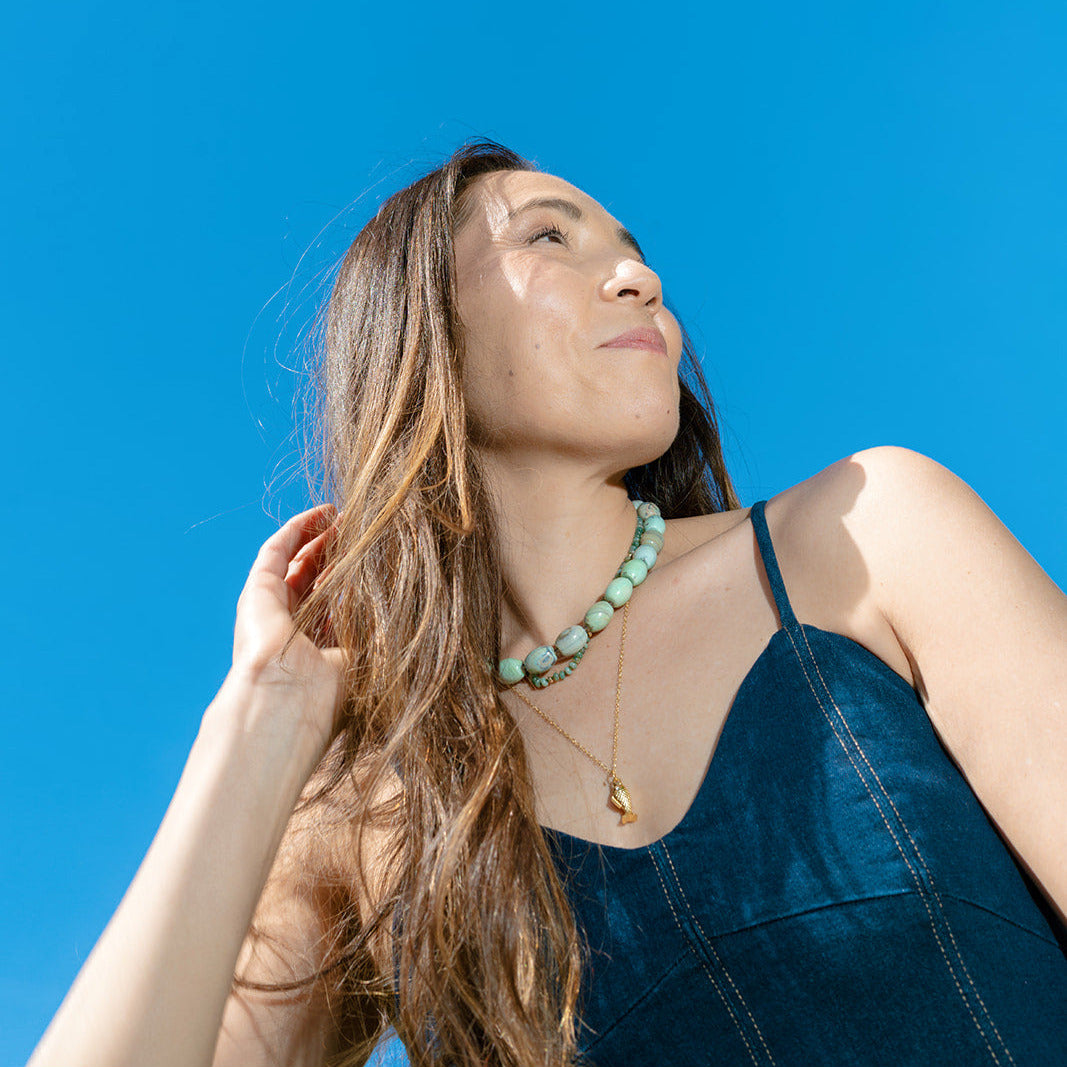 Woman laughing and wearing a teal agate necklace against a clear blue sky