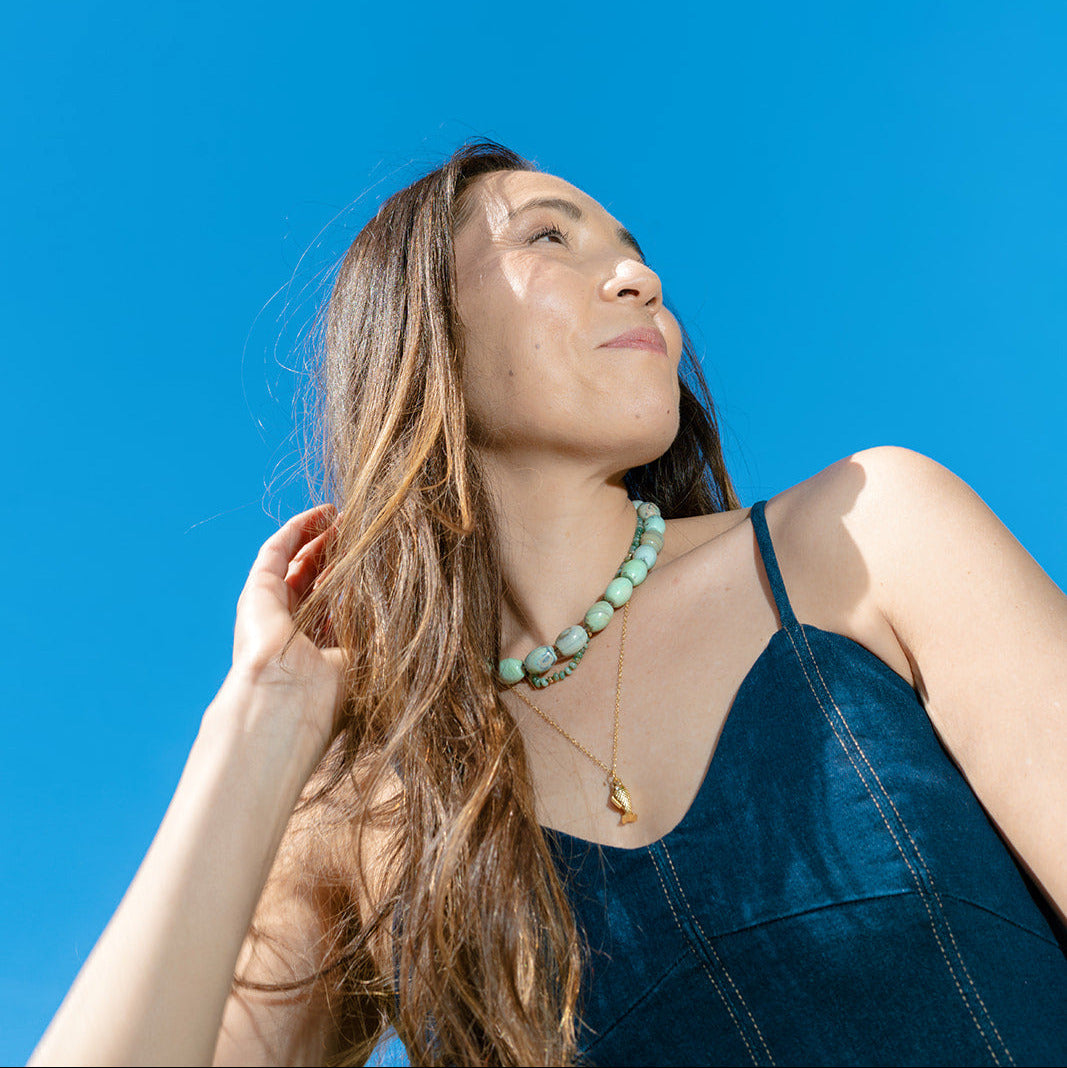 Woman laughing and wearing a teal agate necklace against a clear blue sky