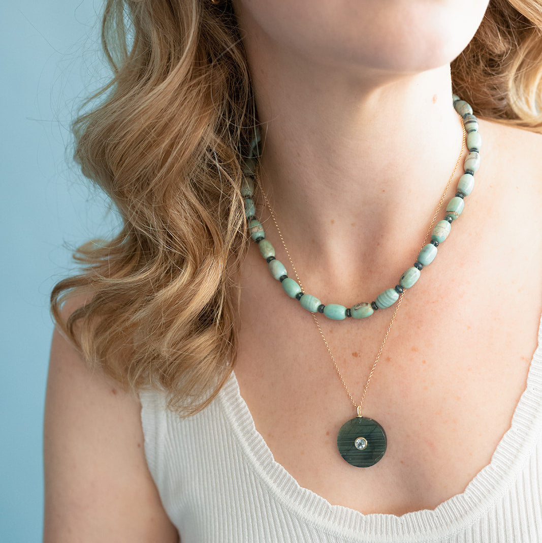 Woman wearing an agate necklace paired with a pendant against a light blue background