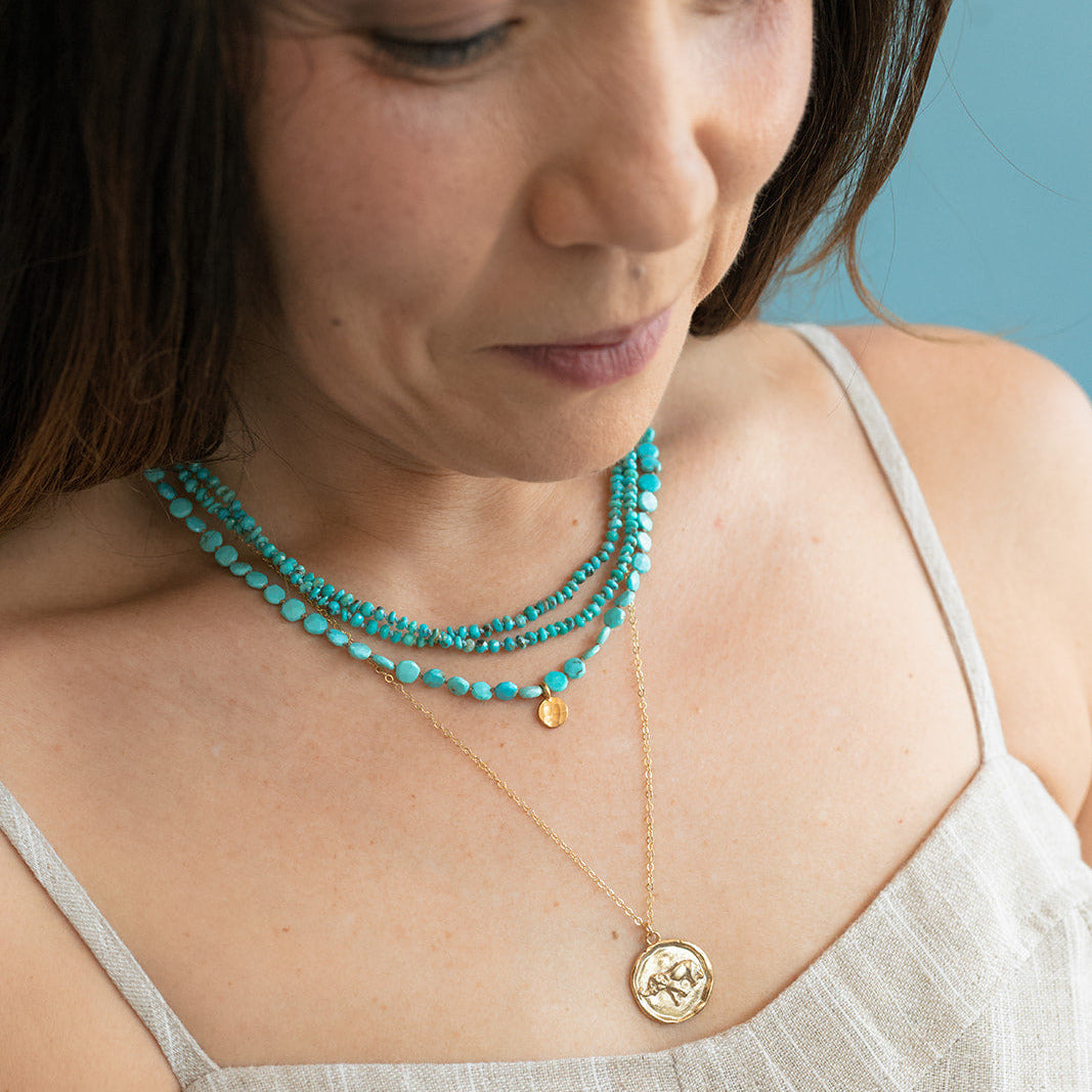 Woman wearing two turquoise necklaces with a tan sundress