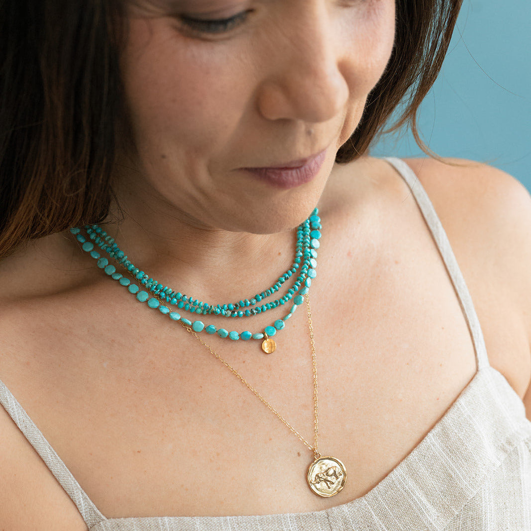 Woman wearing two turquoise necklaces with a tan sundress