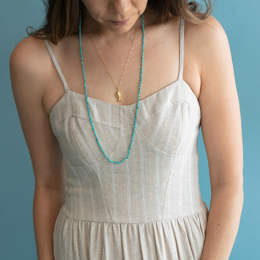 Woman wearing a beige dress with a turquoise necklace against a blue background