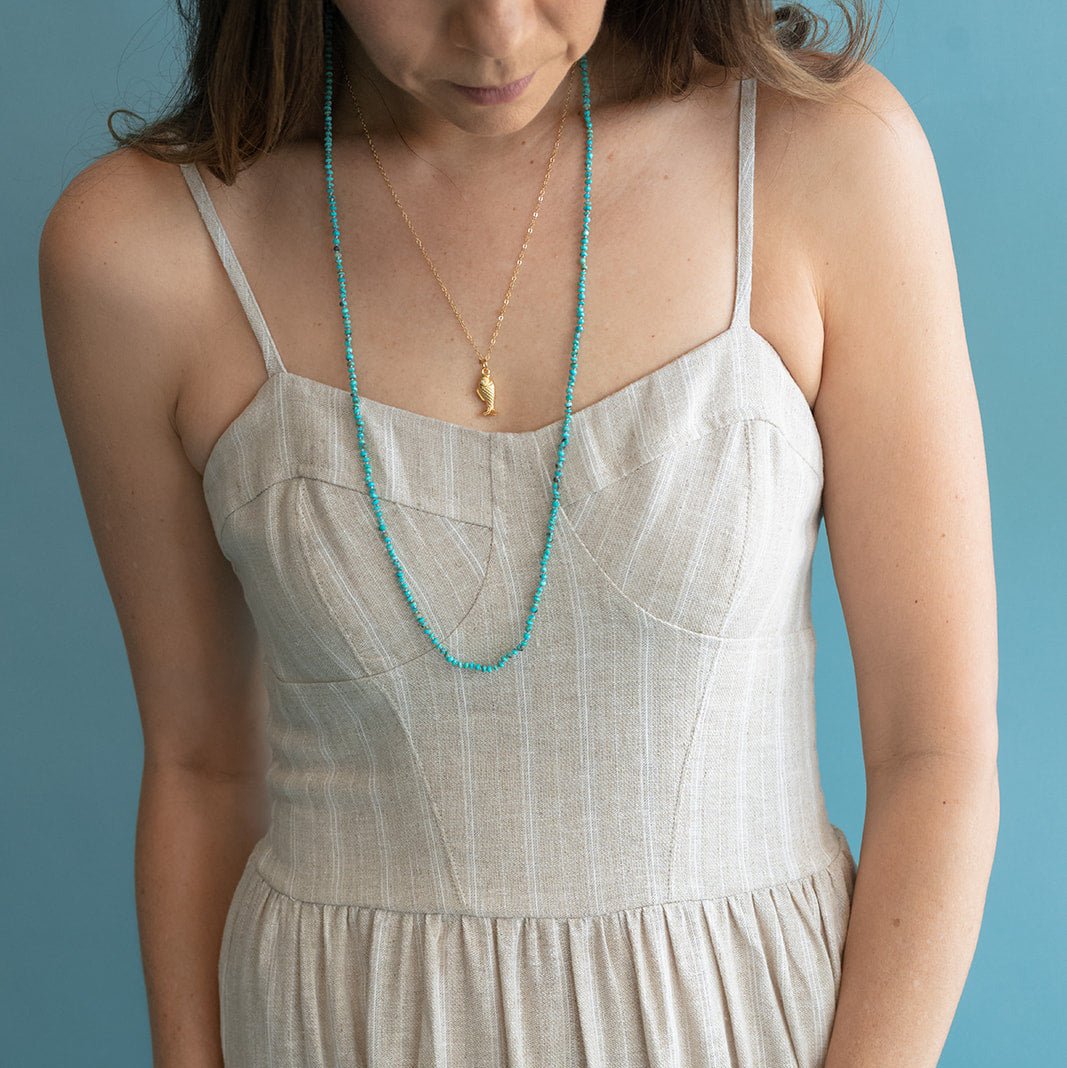 Woman wearing a beige dress with a turquoise necklace against a blue background