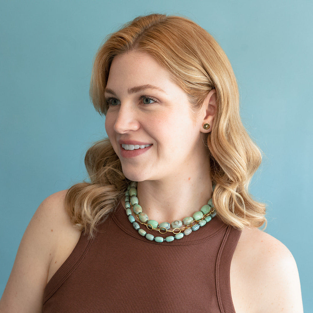 Woman wearing a brown top and teal agate necklace against a light blue background