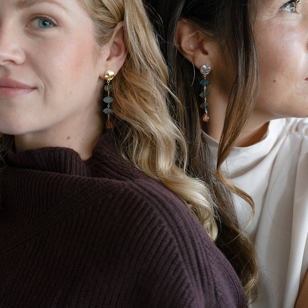 Two women wearing gemstone statement earrings with labradorite and hessian garnet