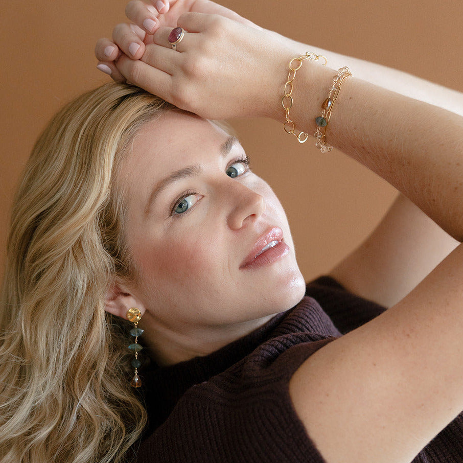 Woman in a brown tank wearing a bracelet stack with a topaz gemstone bracelet