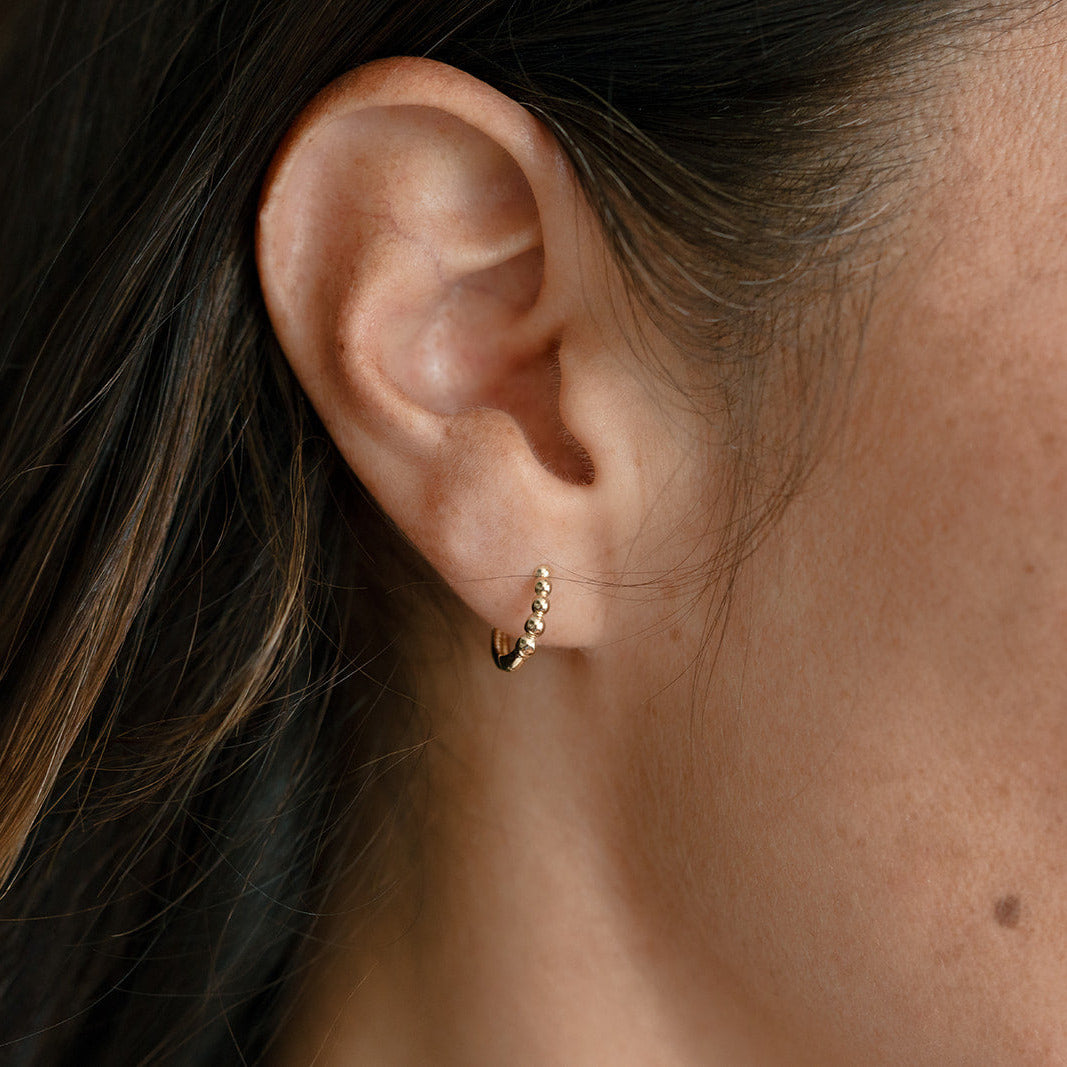 Close up of woman wearing a dainty solid gold huggie earring with beading detail