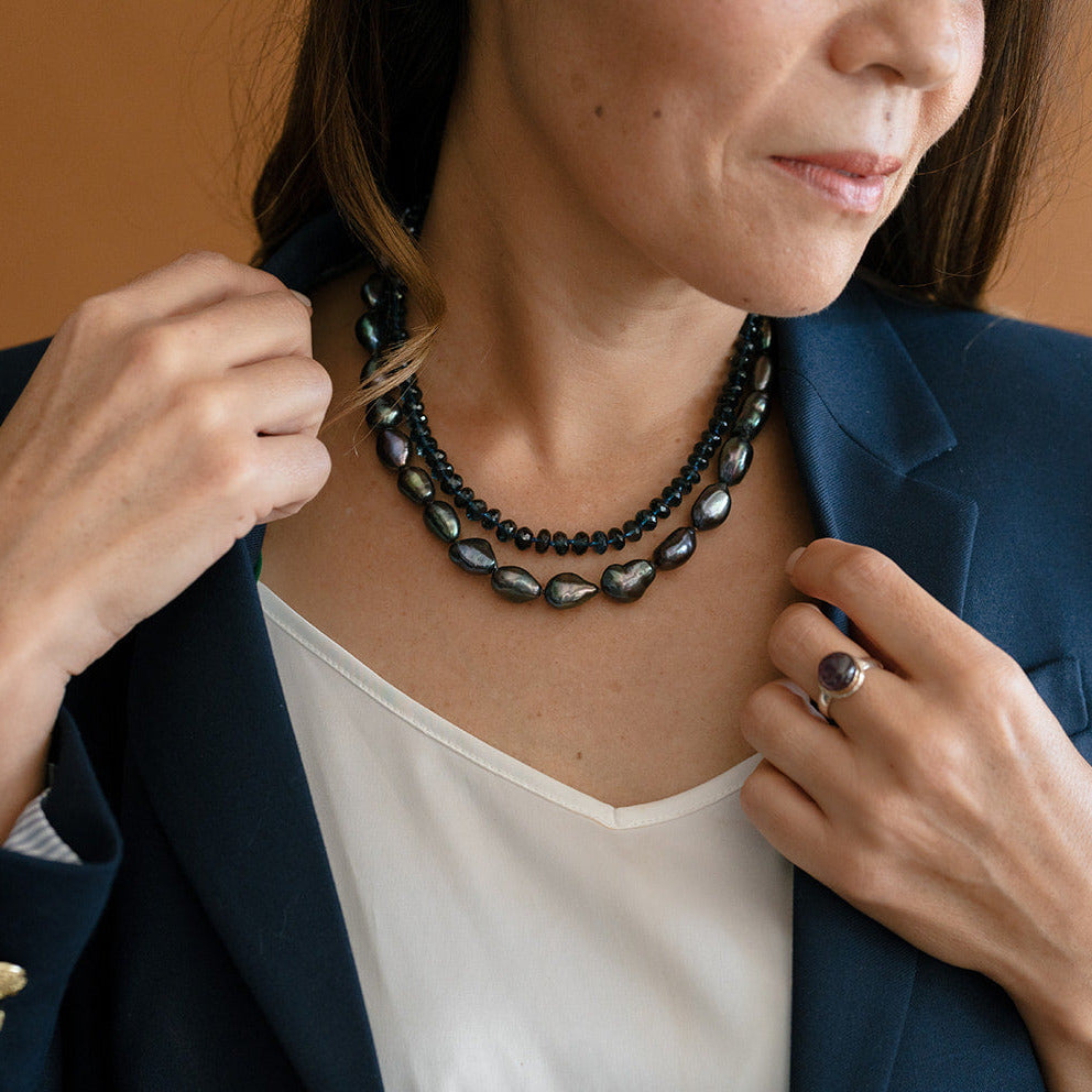 Woman wearing layered peacock pearls layered with a London Blue topaz necklace