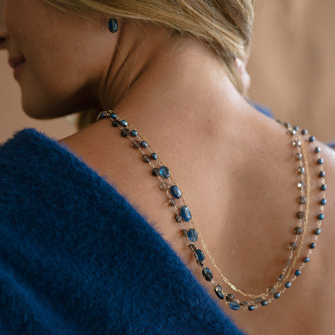 Woman wearing a triple strand necklace draped over her back and wearing a blue sweater