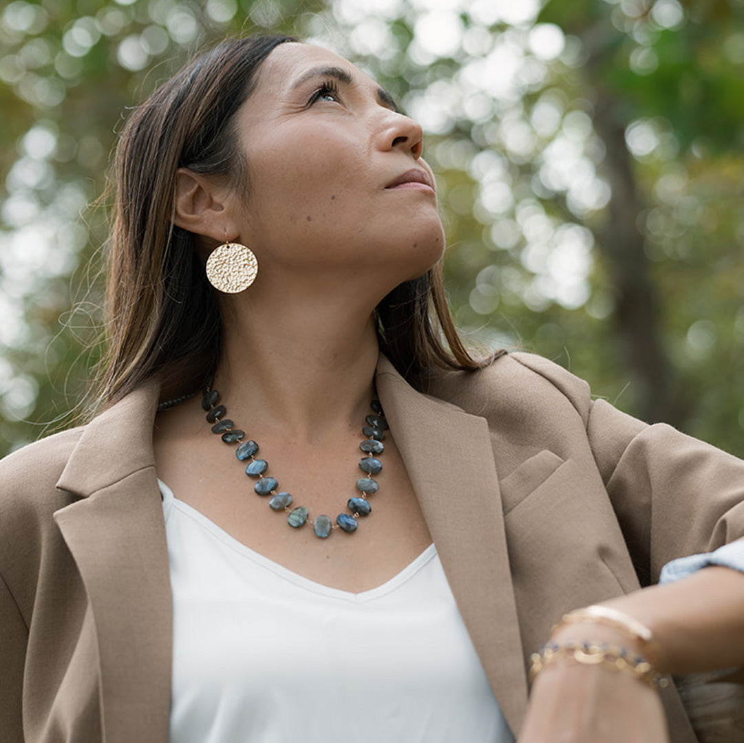 Woman wearing a necklace and earrings outdoors with trees in the background
