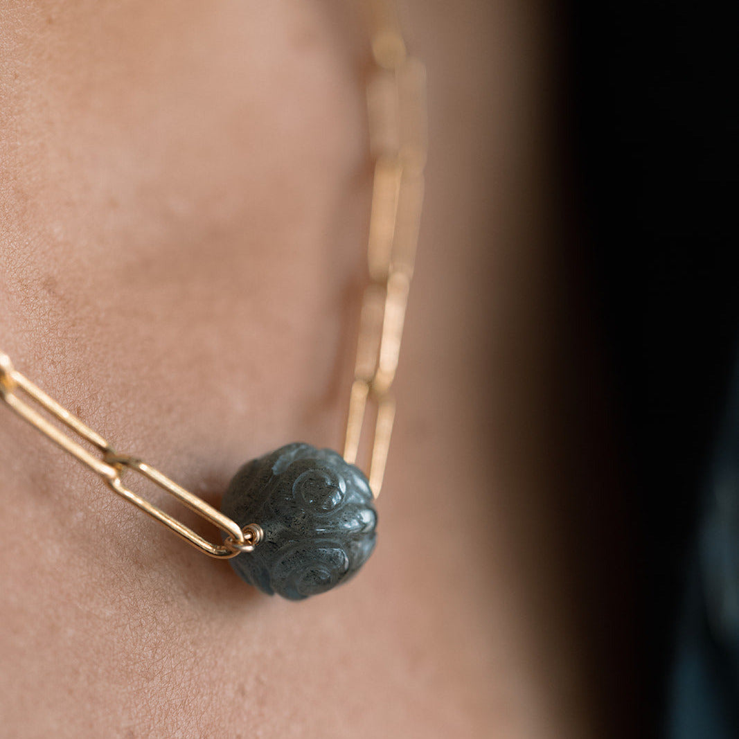Close up of woman wearing gold paperclip chain necklace with a round carved labradorite gem