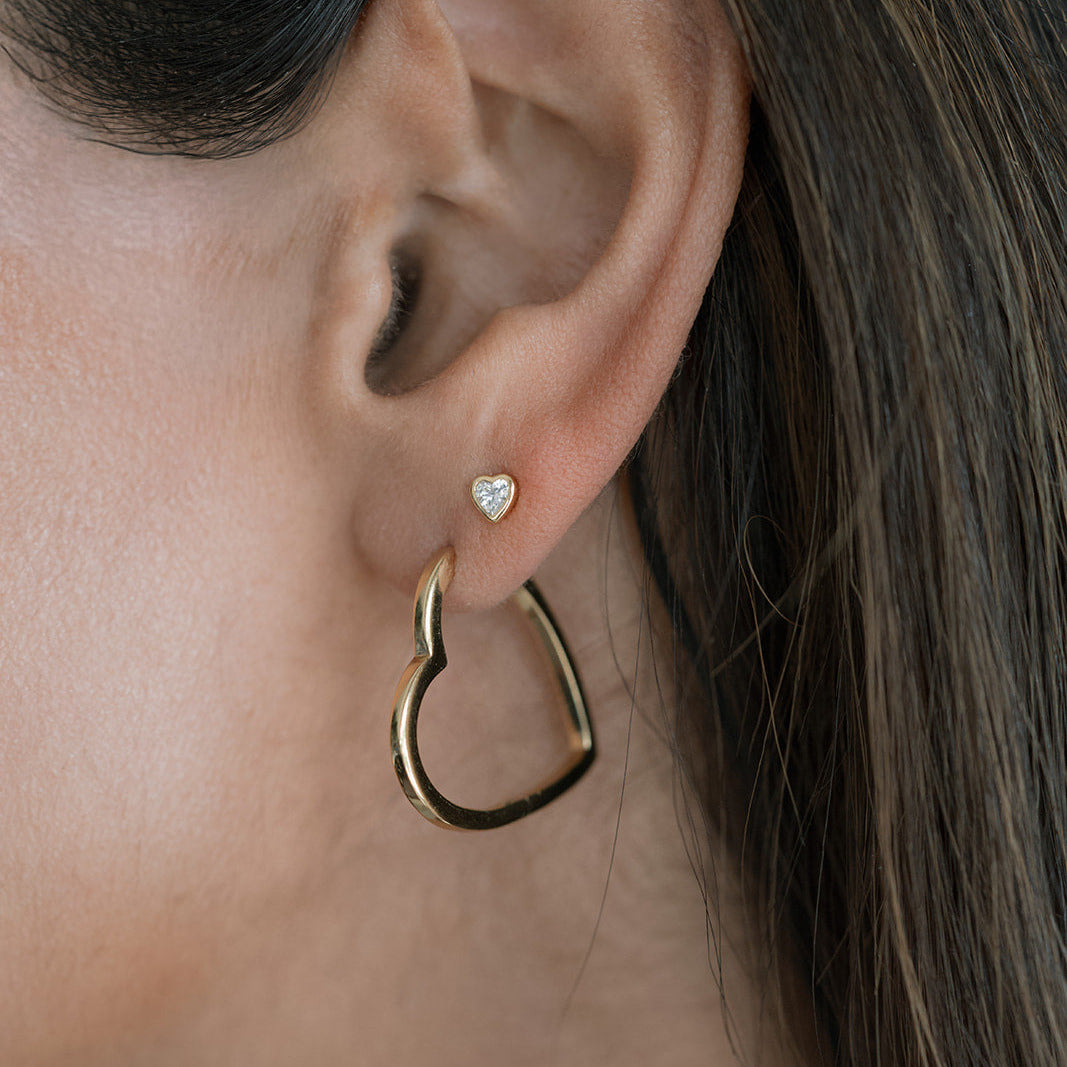 Close-up of a person wearing a gold hoop earring with a heart-shaped stud.