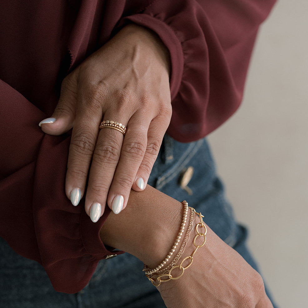 Close-up of a person's hands wearing gold bracelets and rings, with a blurred background.