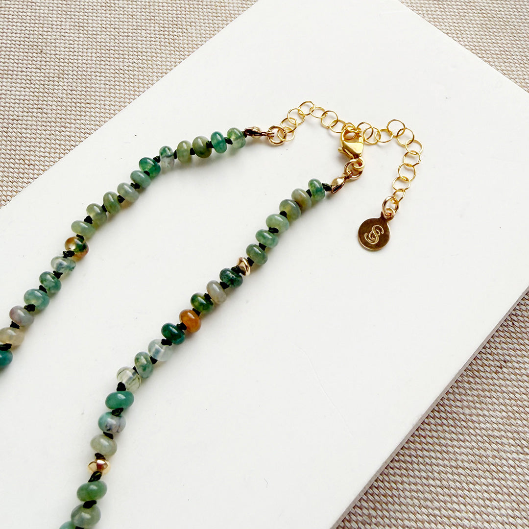 Necklace with small green agate and gold beads on a white surface