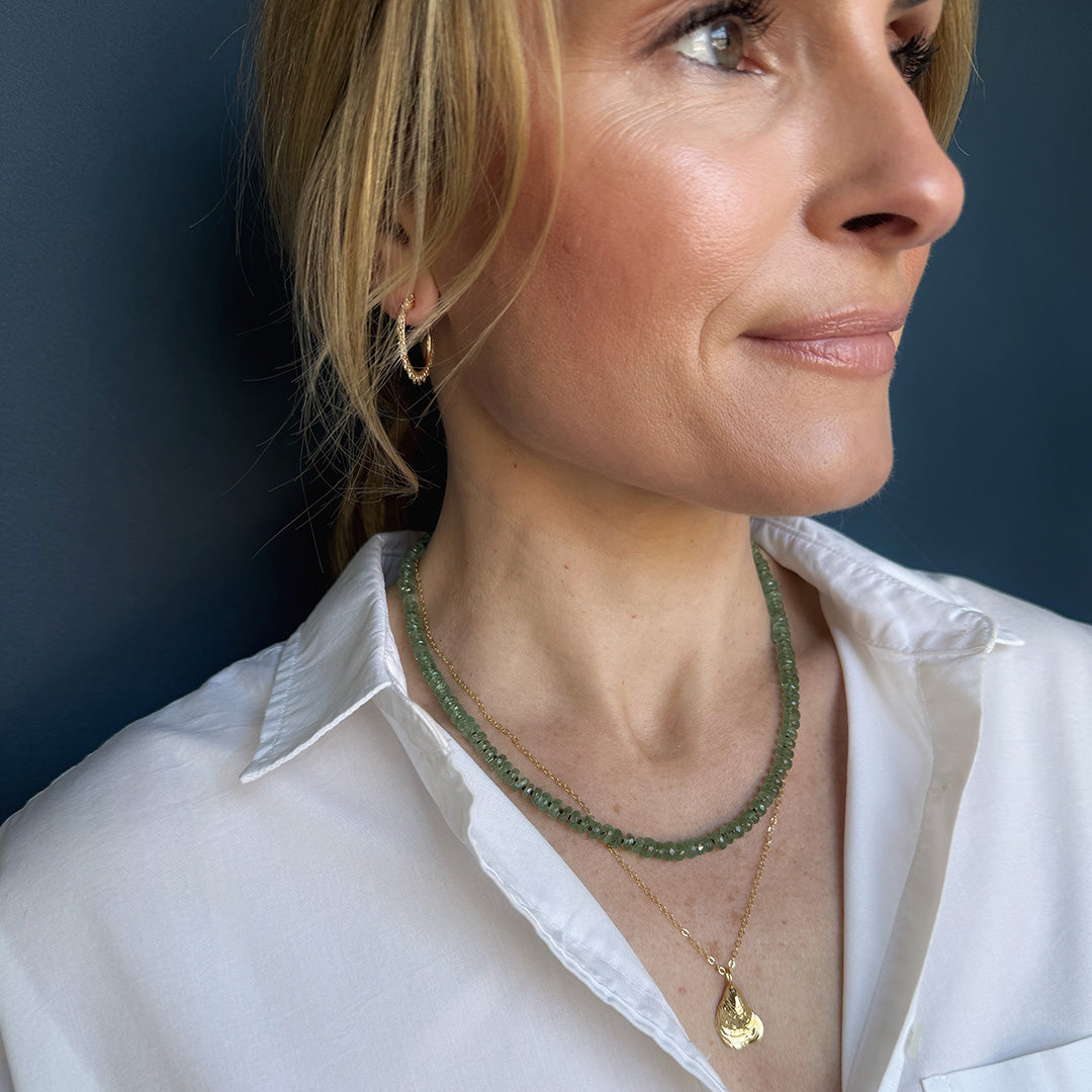 Person wearing a green kyanite gemstone necklace and gold pendant with a white shirt.