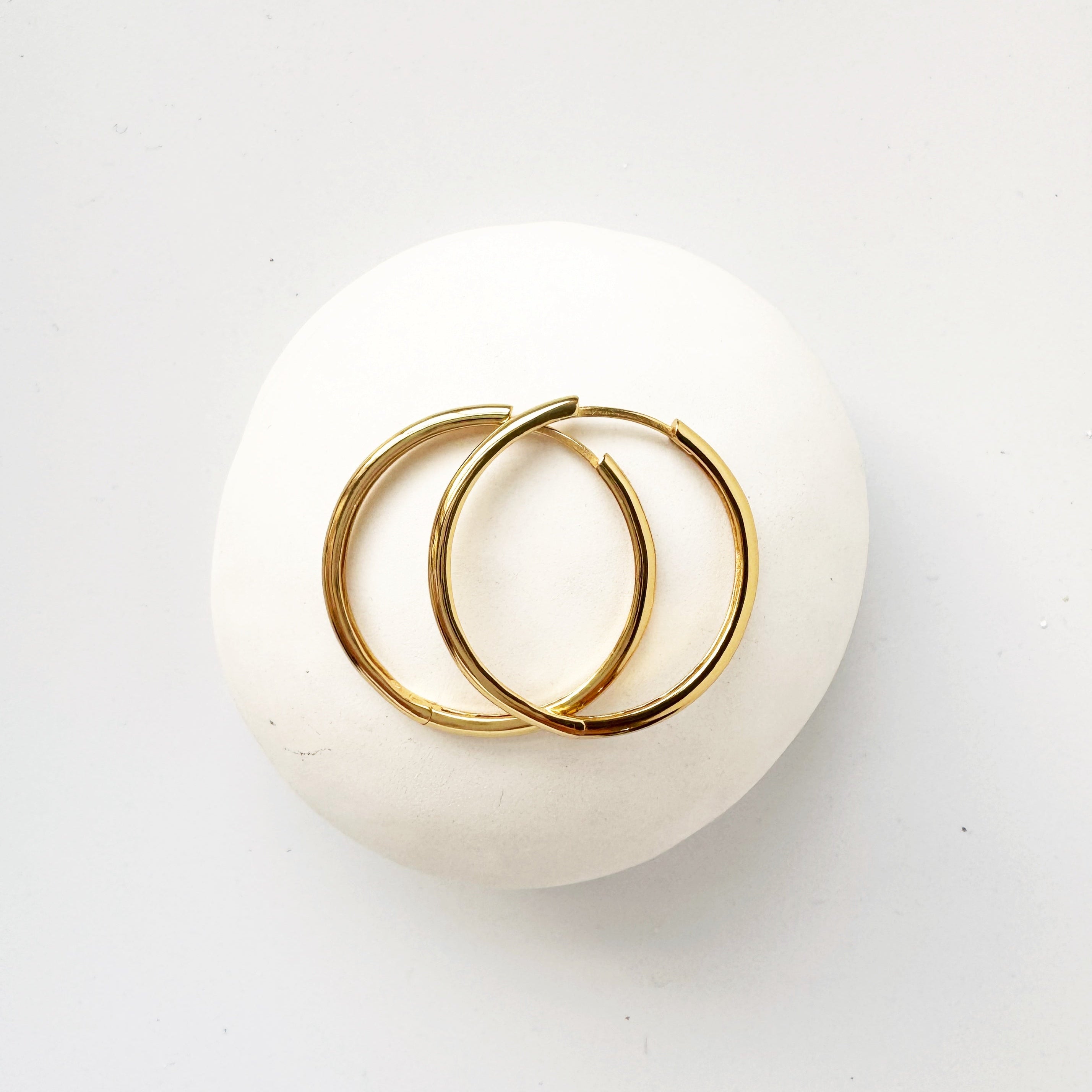 A pair of gold hoop earrings placed on a white surface.
