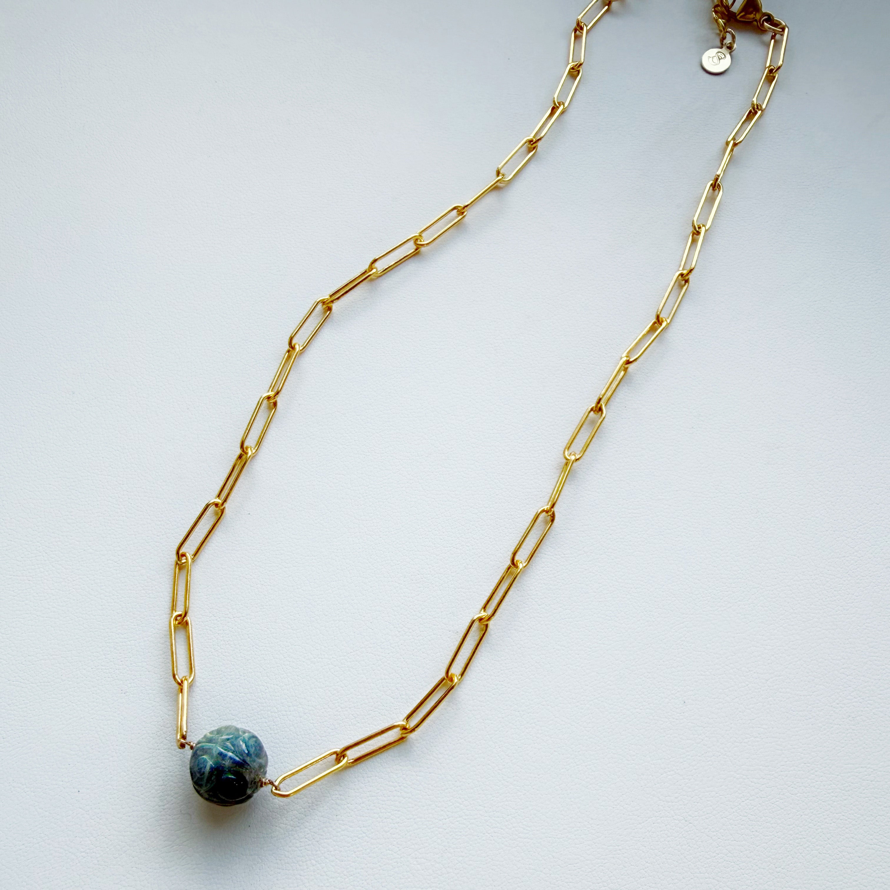 Gold paperclip chain necklace with a round carved labradorite gem on a white background