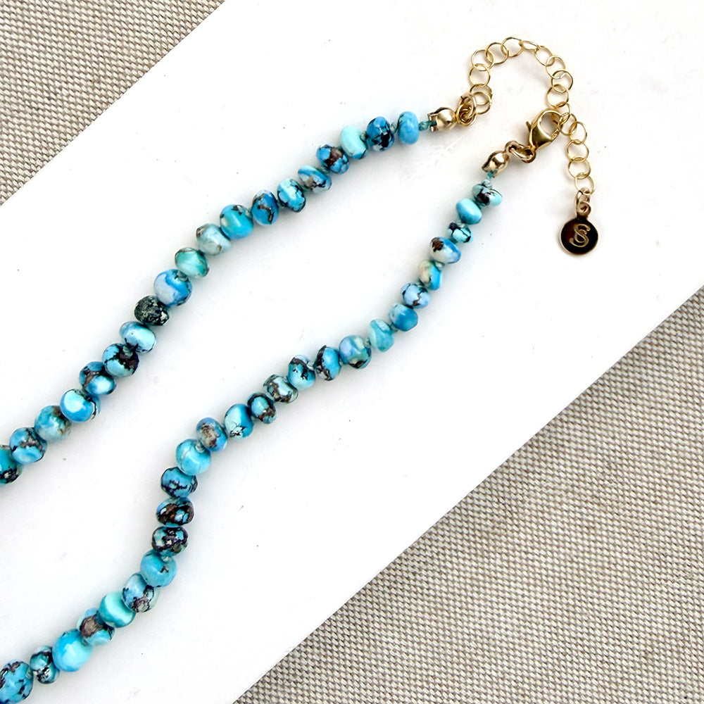 Clasp detail of knotted Golden Hills turquoise necklace, draped over a white plate on a neutral textured surface.