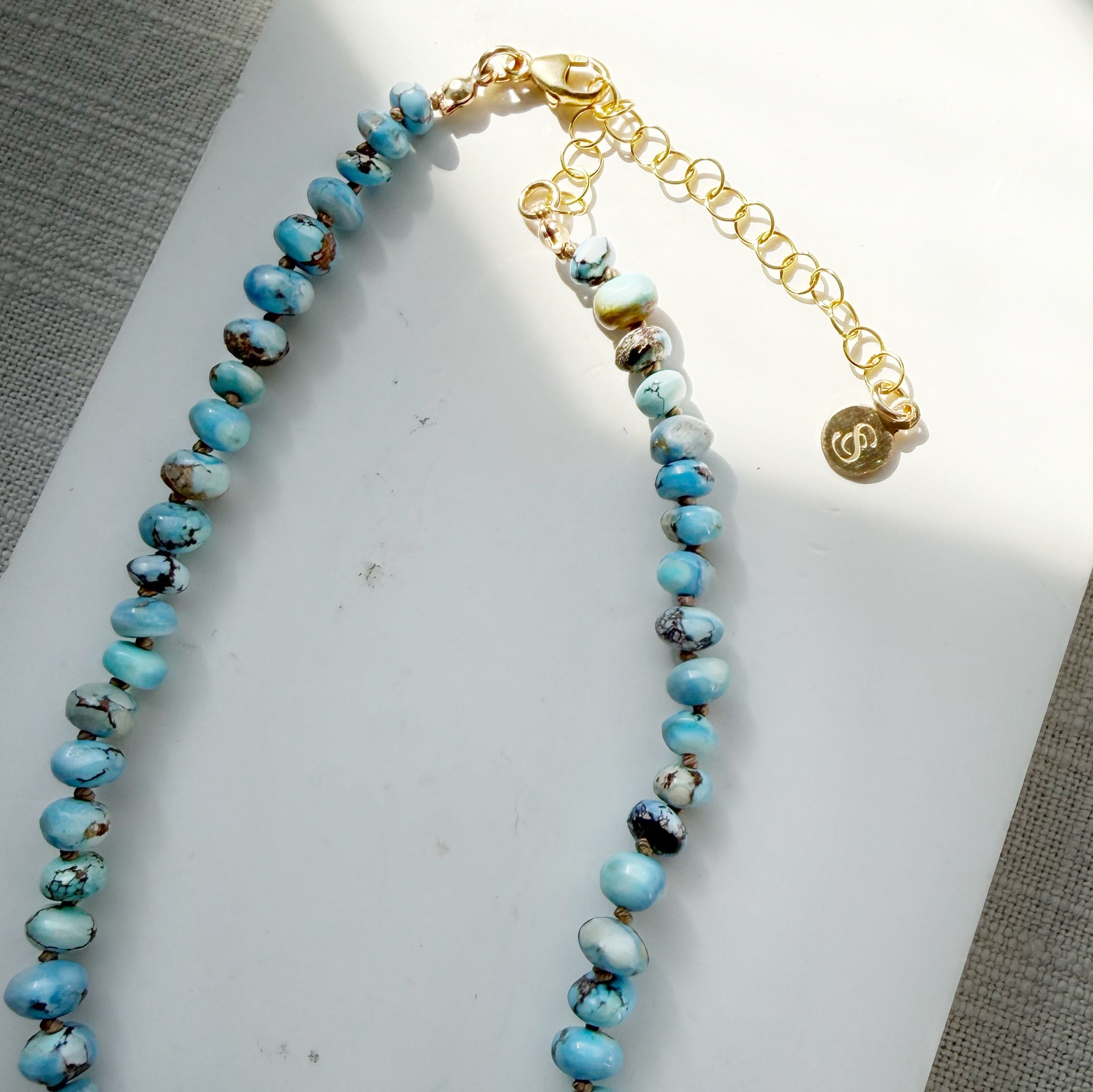 Necklace with Golden Hills turquoise beads on a white dish against a gray background