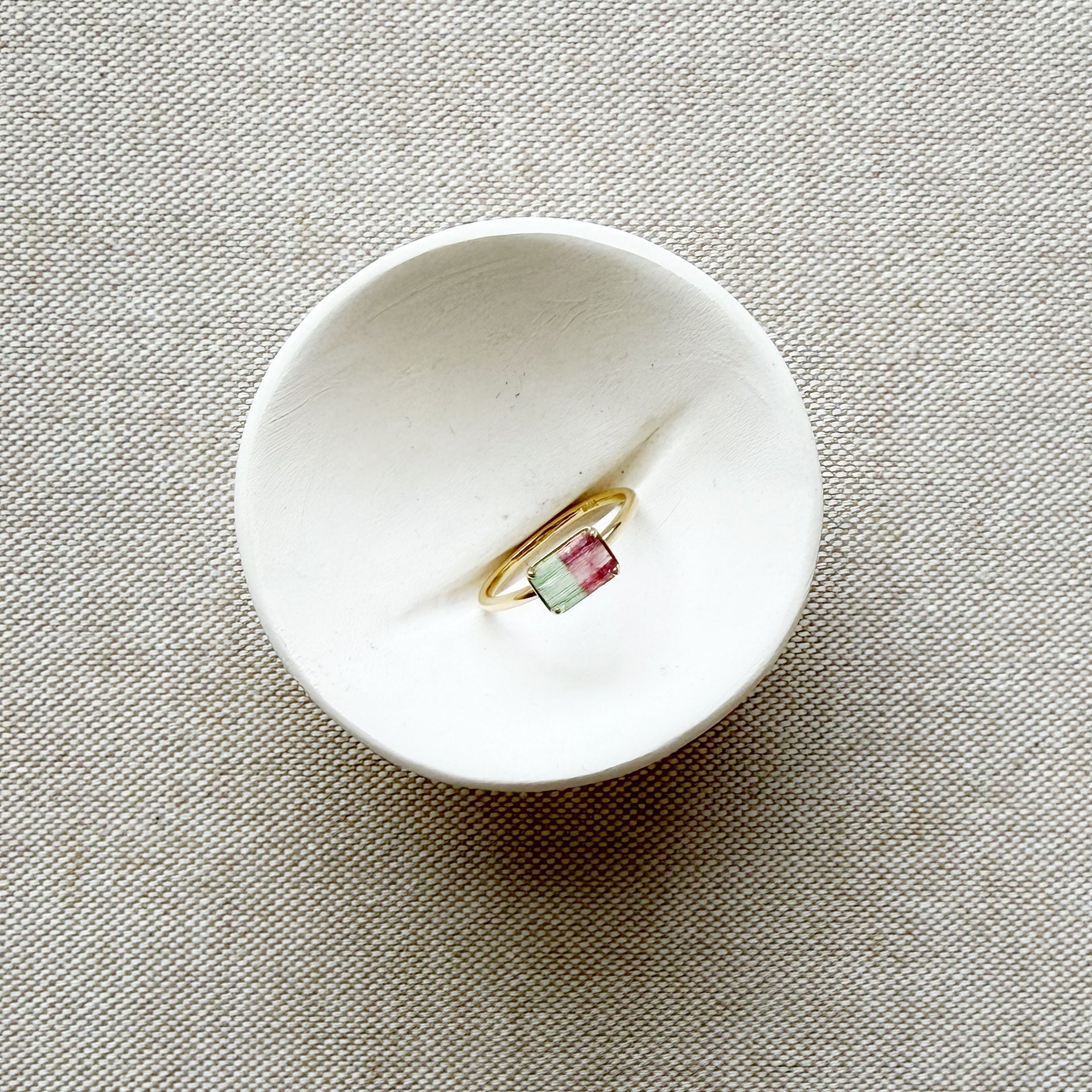 Gold ring with a green gemstone in a white dish on a beige fabric background