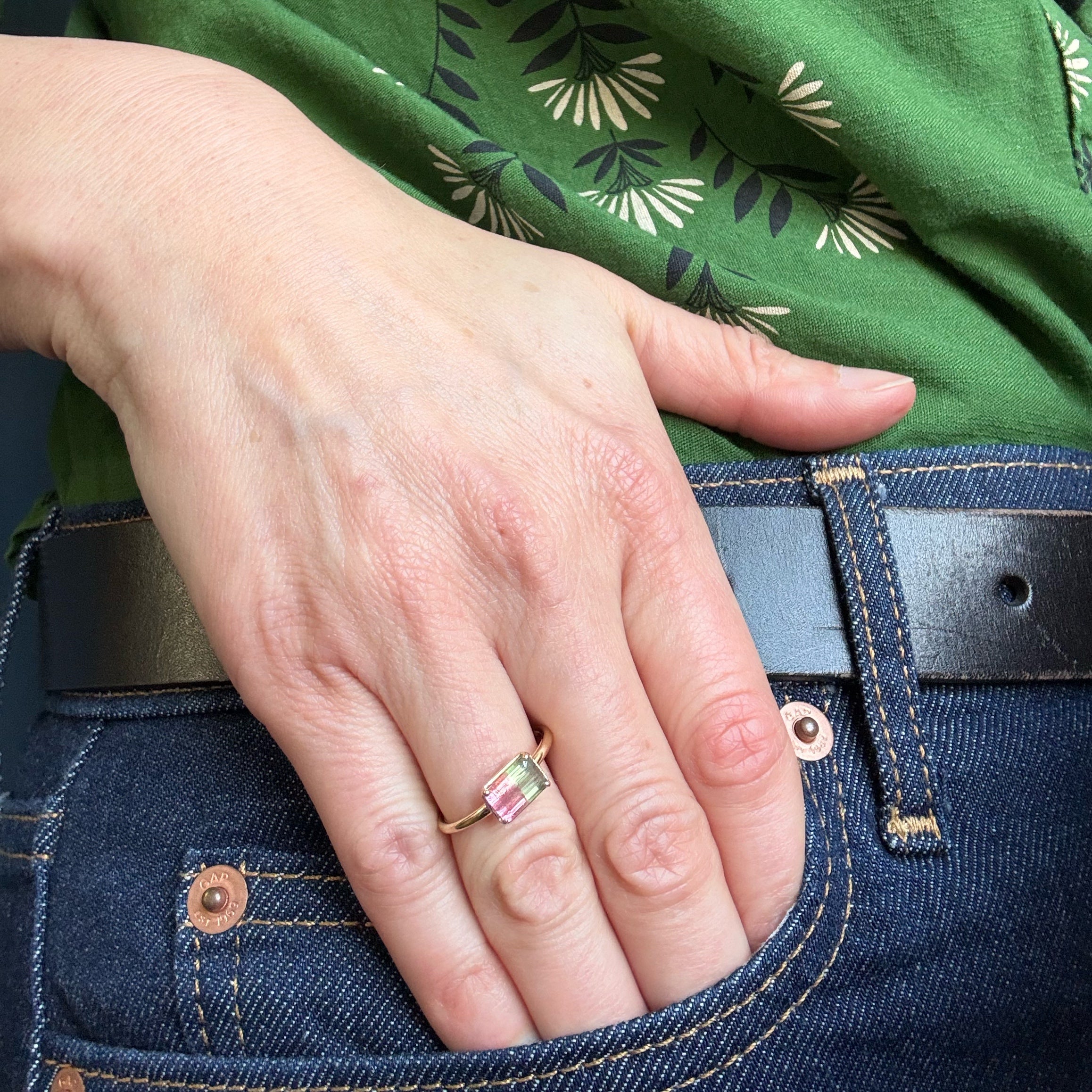 Hand with a ring in a pocket, wearing a green shirt with a floral pattern.
