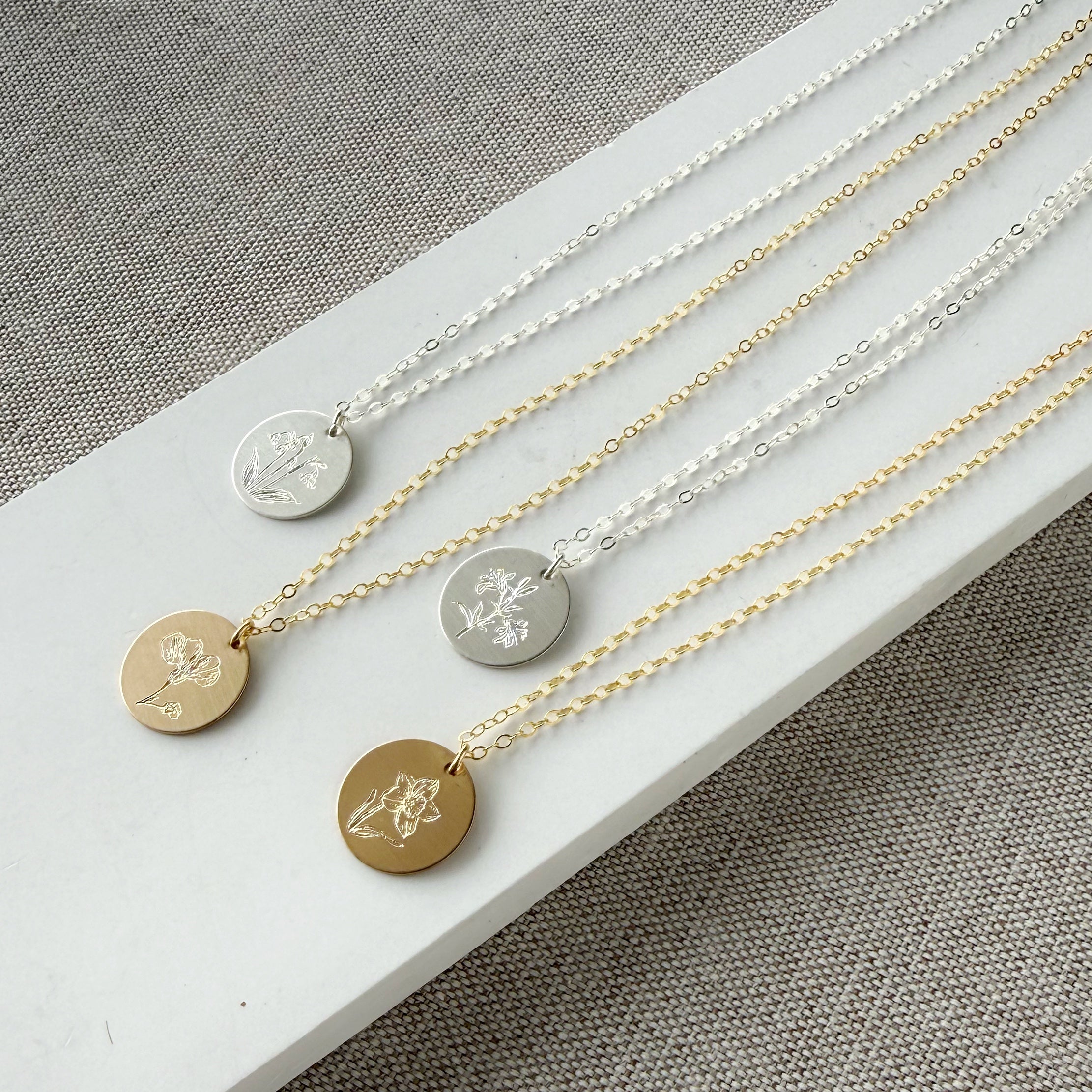 Four necklaces with circular pendants featuring engraved flower designs on a white surface.