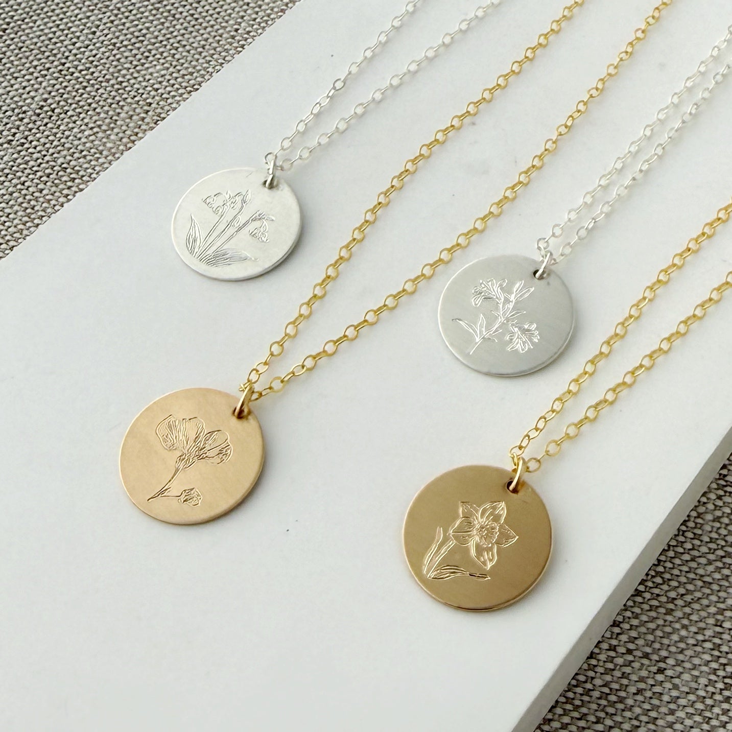 Four necklaces with circular pendants featuring engraved flower designs on a white surface.