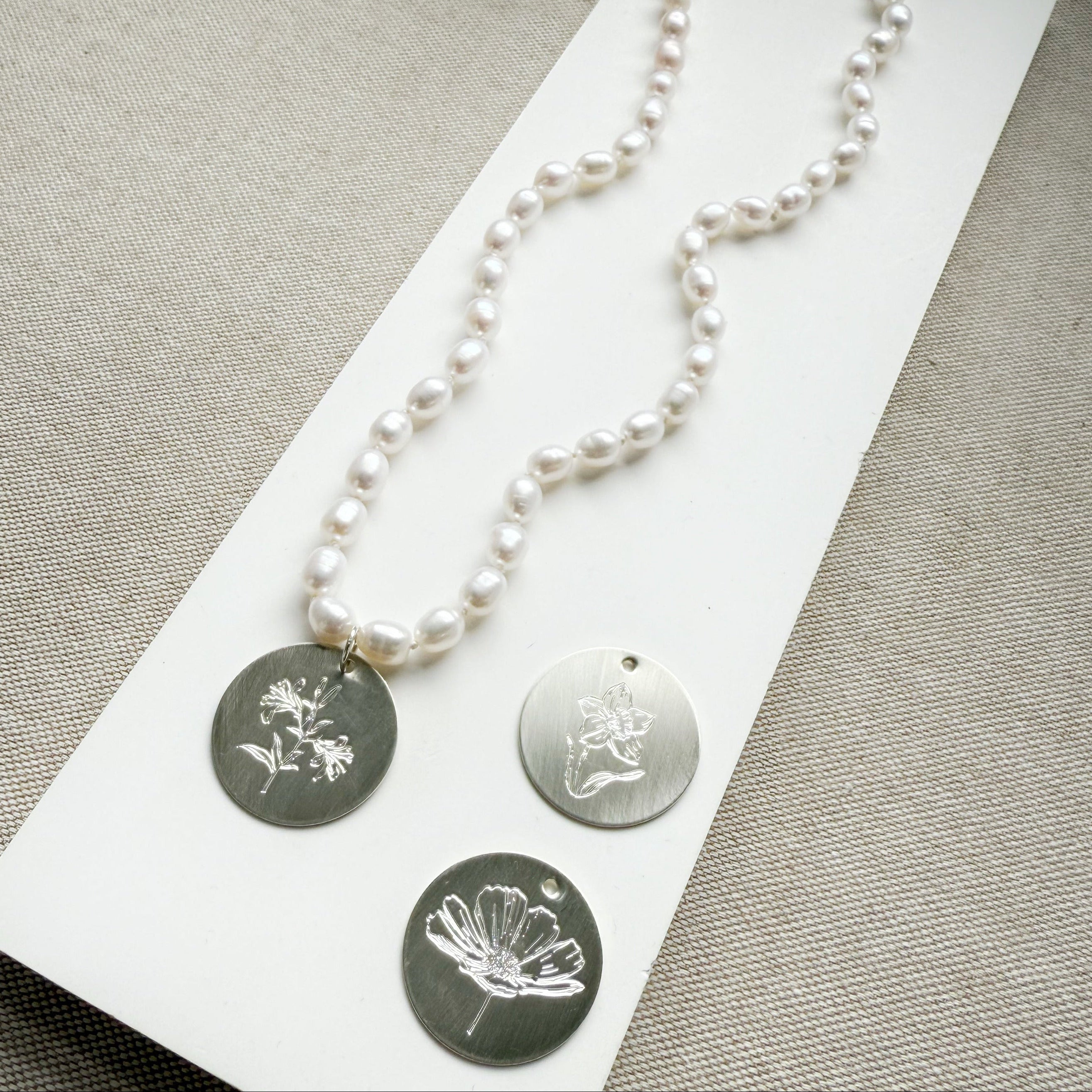 Pearl necklace with three silver pendants on a gray surface