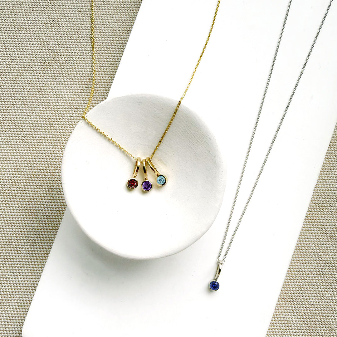 Two necklaces with gemstone pendants on a textured surface