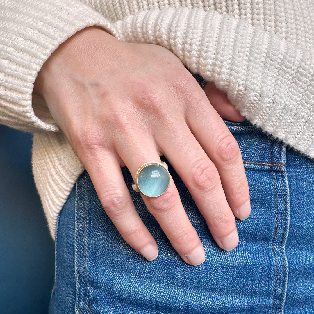 Hand wearing a round blue aquamarine ring on a blue background