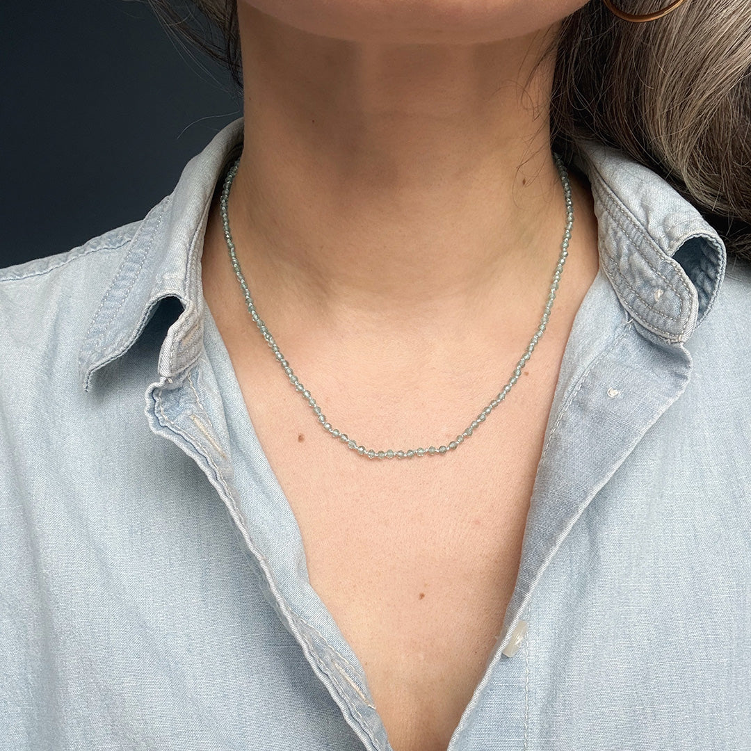 Person wearing an apatite gemstone knotted necklace with a light blue denim shirt