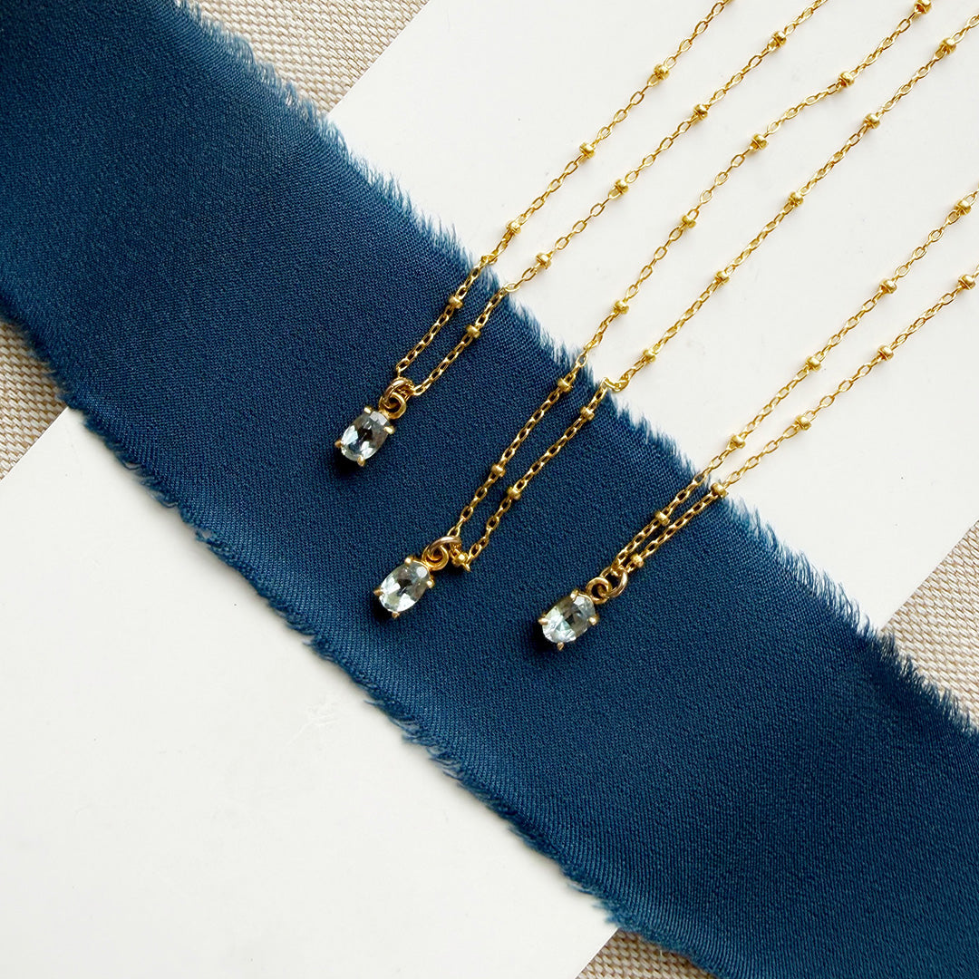 Three gold necklaces with a blue gemstone pendant on a blue ribbon