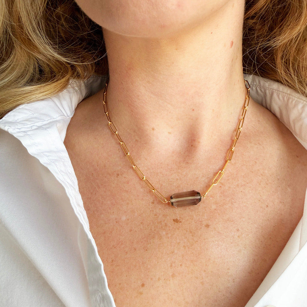 Close up of woman wearing a white shirt with a gold necklace and faceted smokey quartz pendant