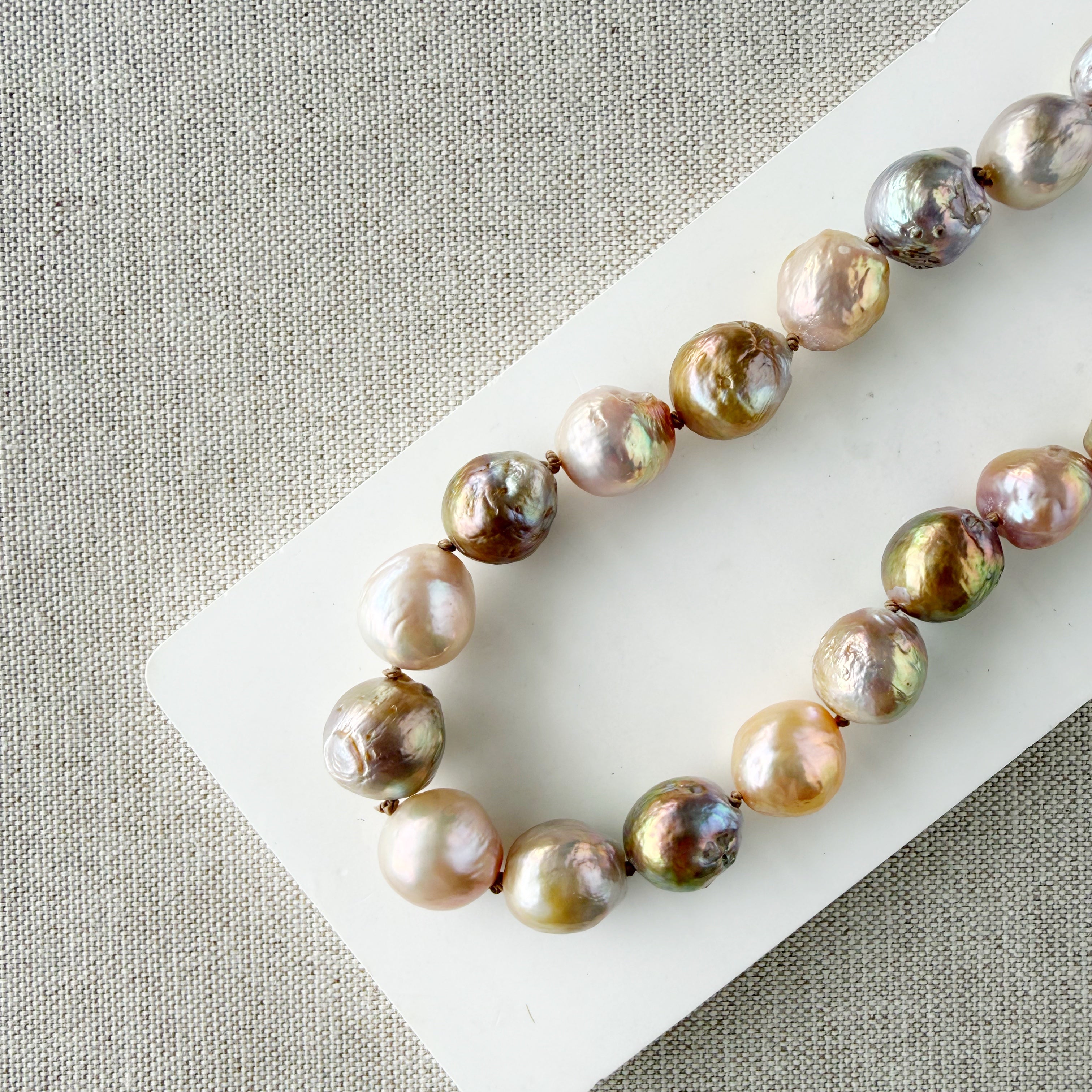 Champagne and rose baroque pearl necklace on a white dish and textured beige background