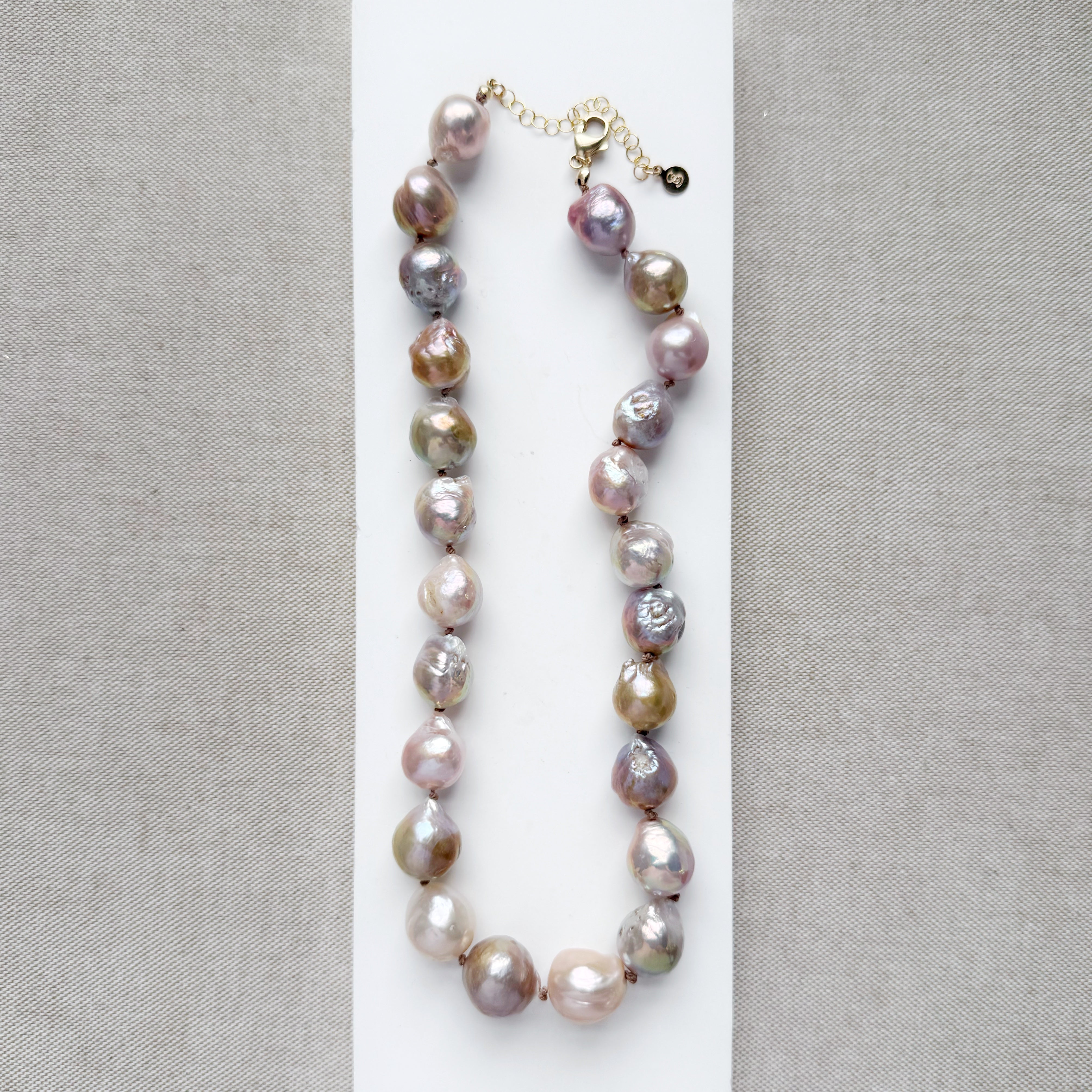 Champagne and rose baroque pearl necklace on a white dish and textured beige background