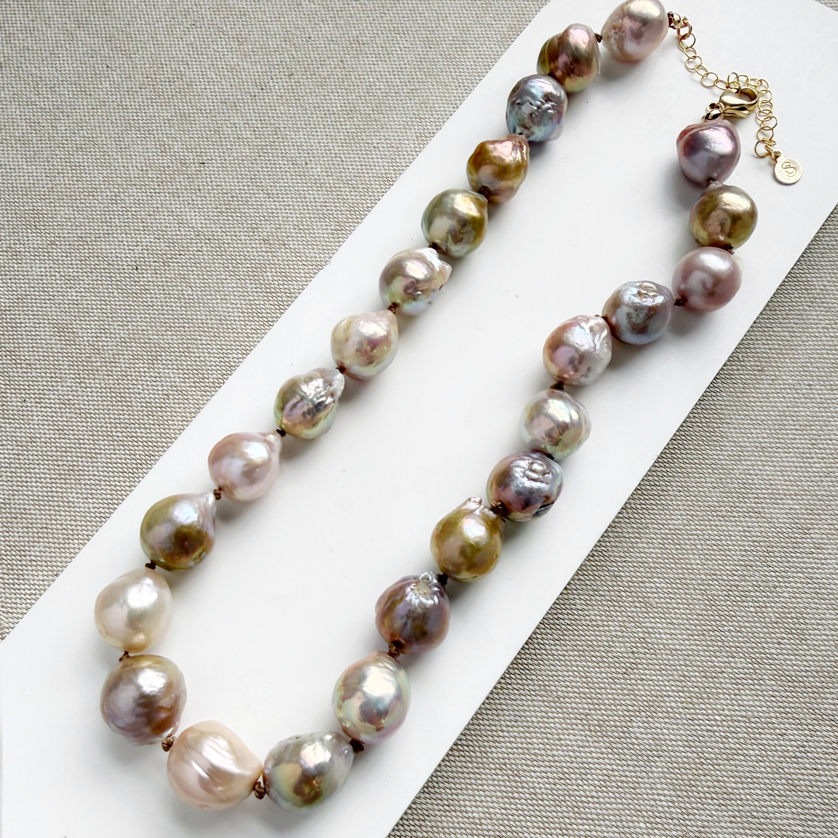 Champagne and rose baroque pearl necklace on a white dish and textured beige background