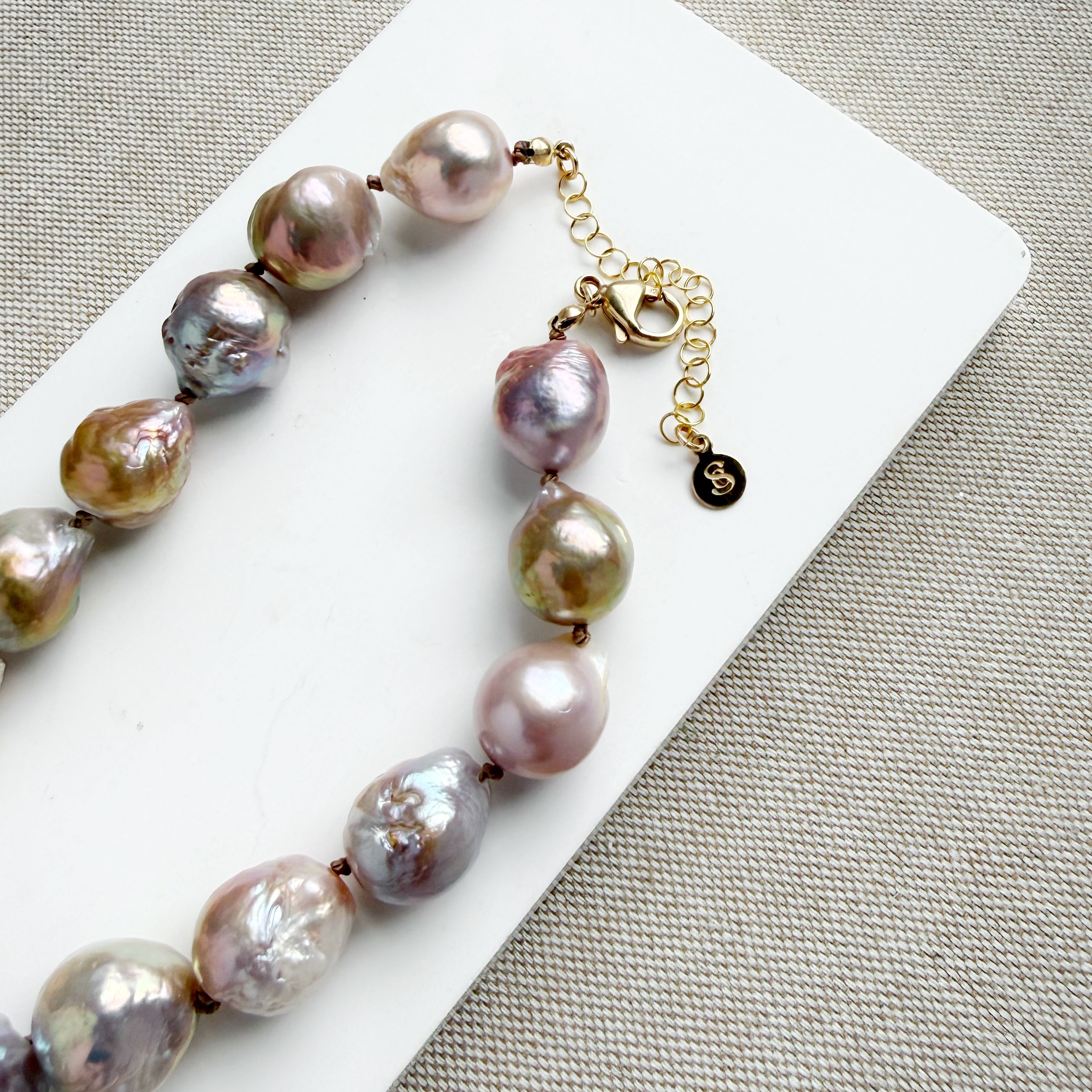 Champagne and rose baroque pearl necklace on a white dish and textured beige background