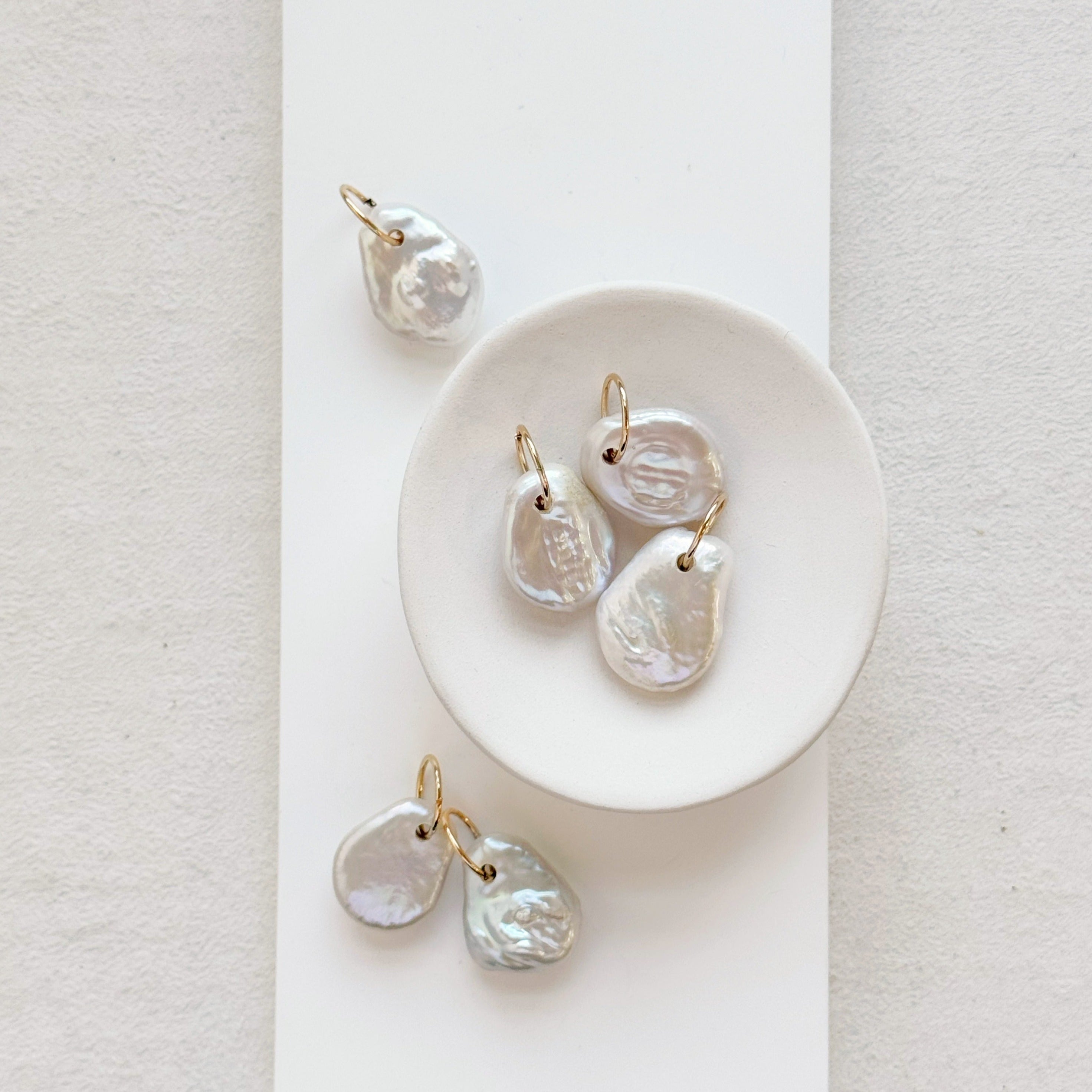 Keshi pearl charm with large gold ring in a white dish.