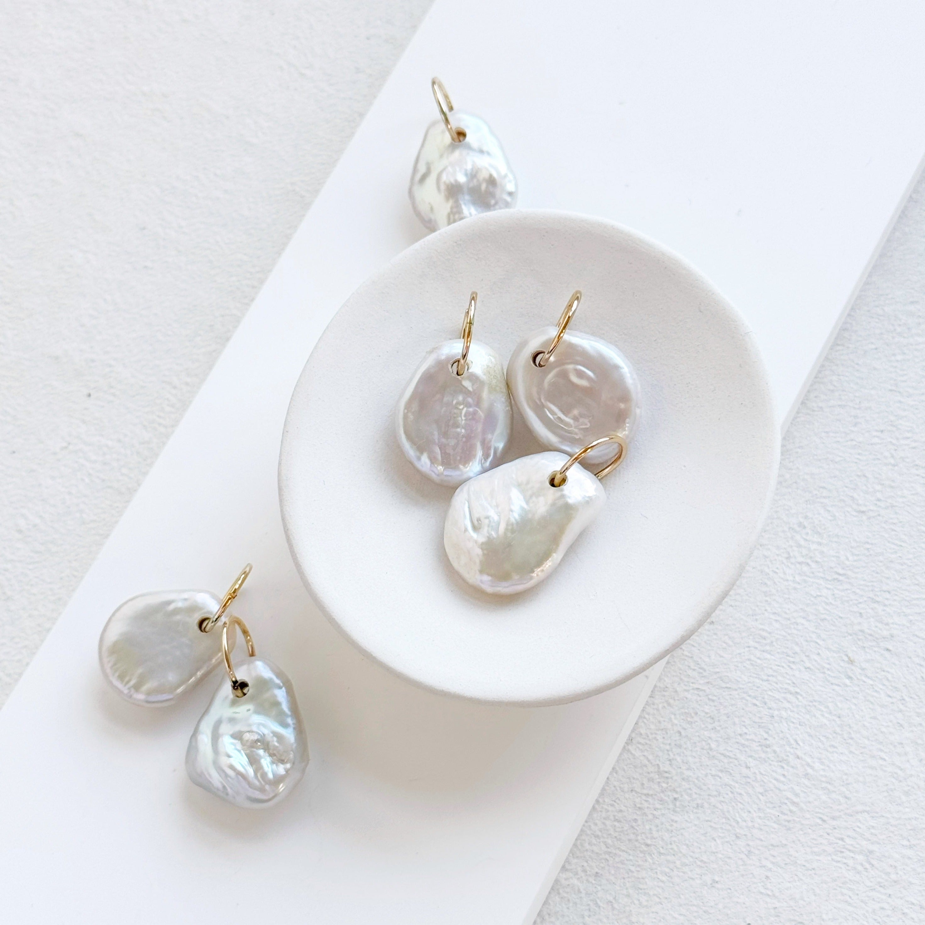 Keshi pearl charm with large gold ring in a white dish.