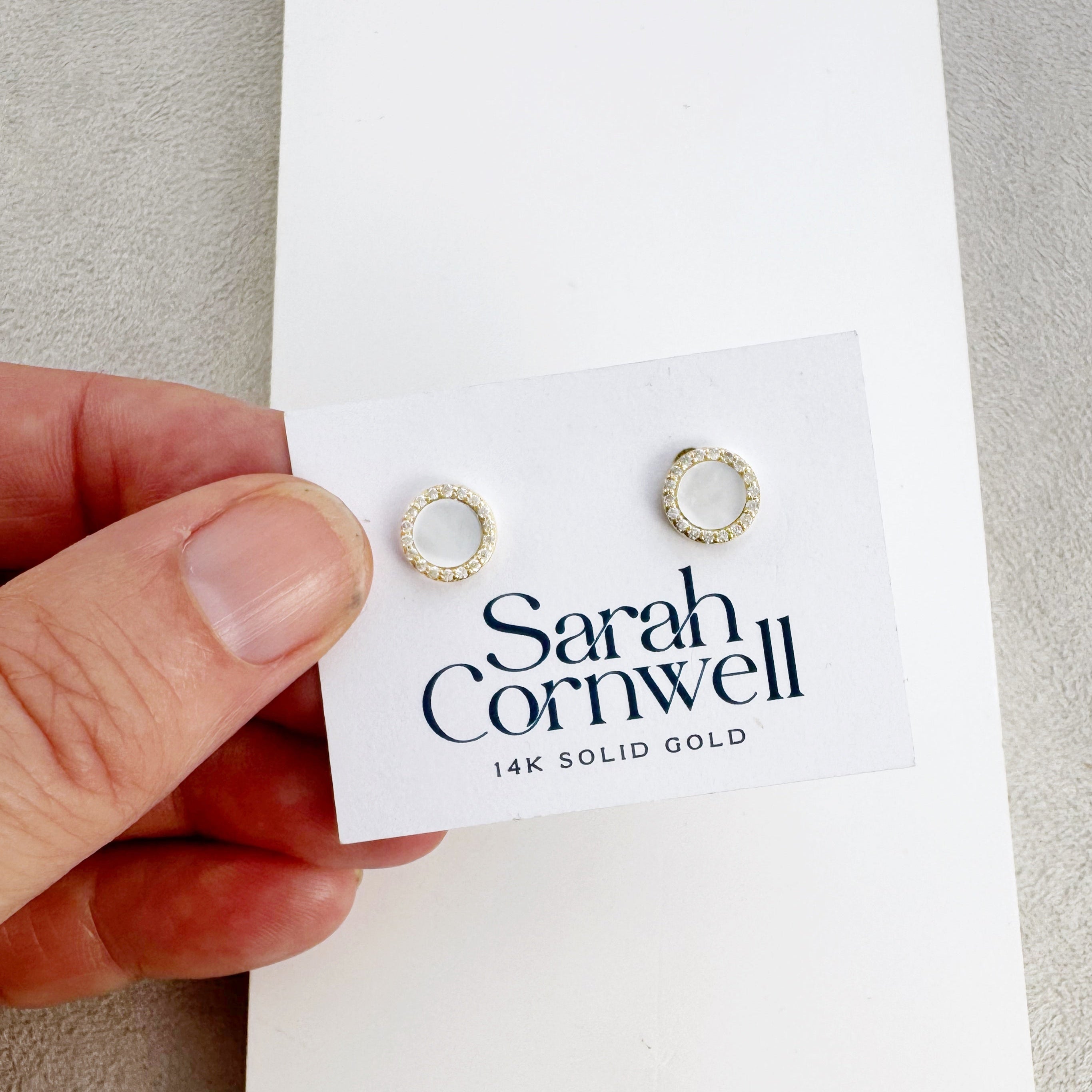 Gold earrings on a Sarah Cornwell branded card held by a hand.