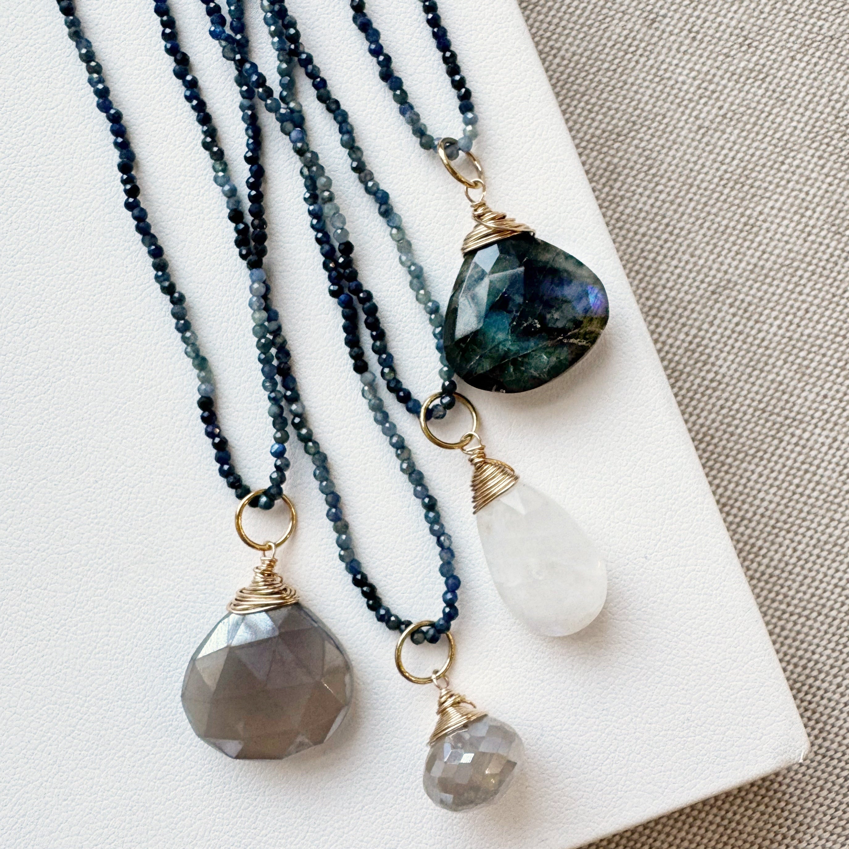 Three necklaces with stone pendants on a beige surface