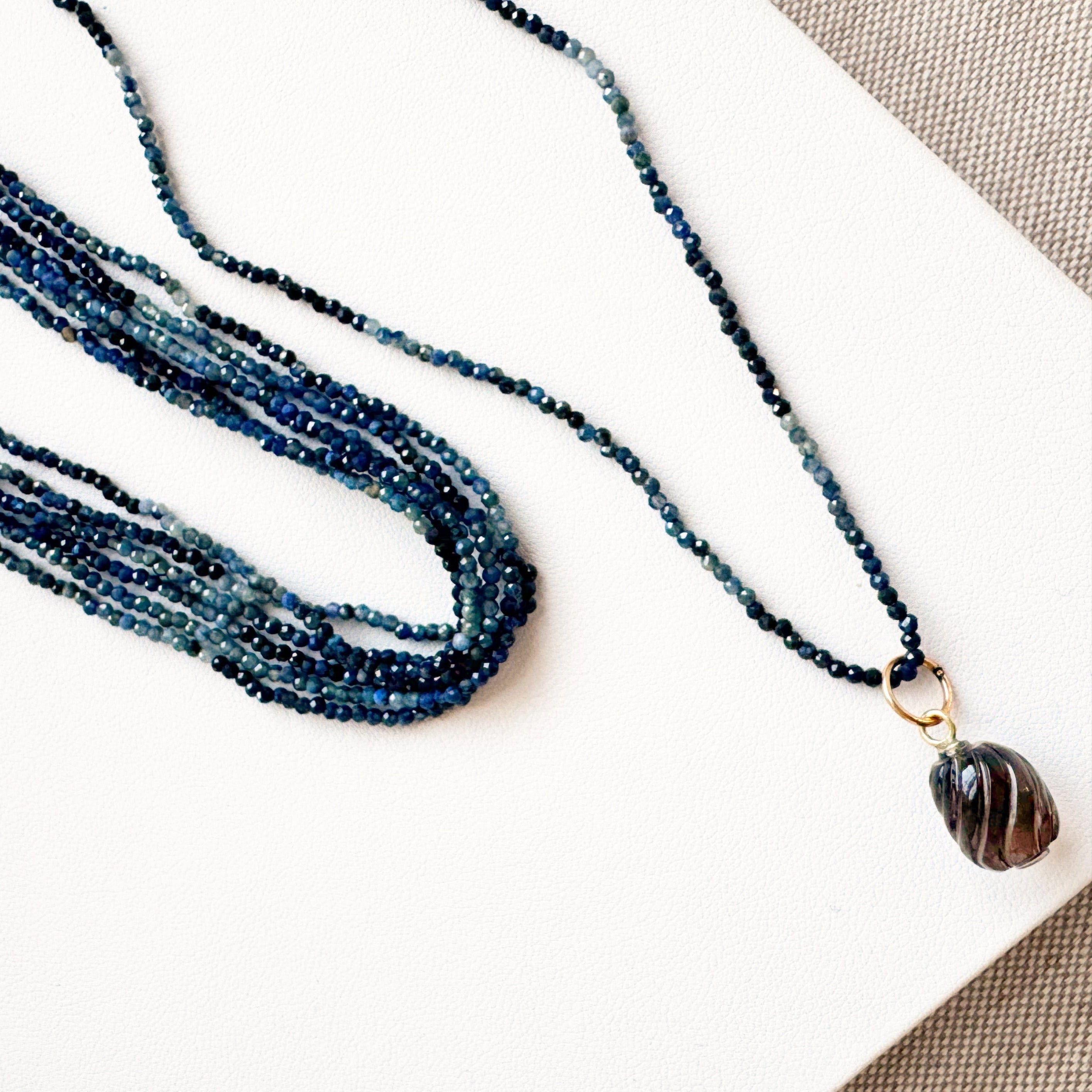 Blue beaded necklace with a striped pendant on a white surface