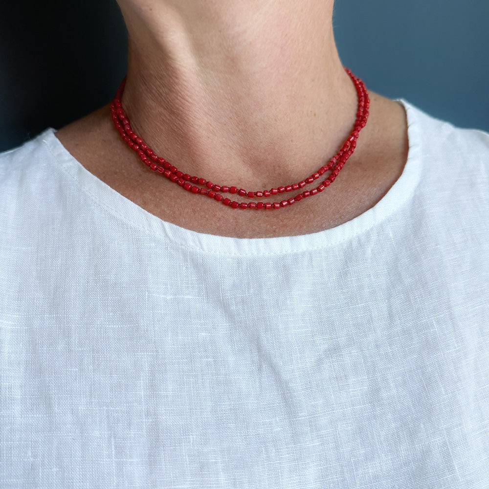 Woman wearing white tank with a long knotted necklace made of small coral beads