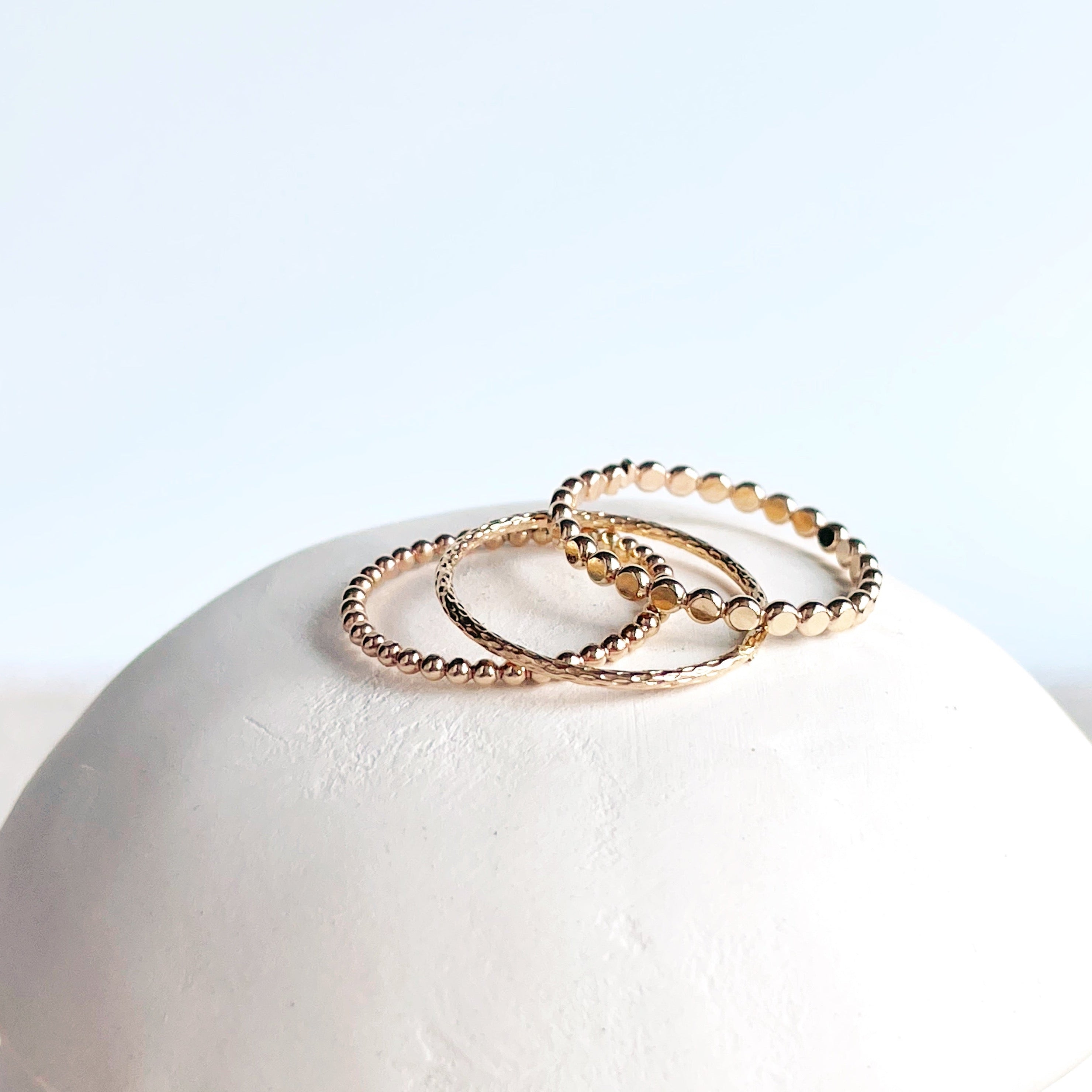 A stack of three gold beaded rings with a textured surface, displayed on a white marble surface.